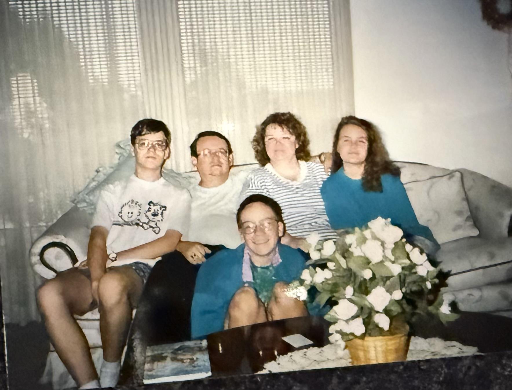 A family sits together on a couch in a well-lit living room, sharing smiles and moments.
