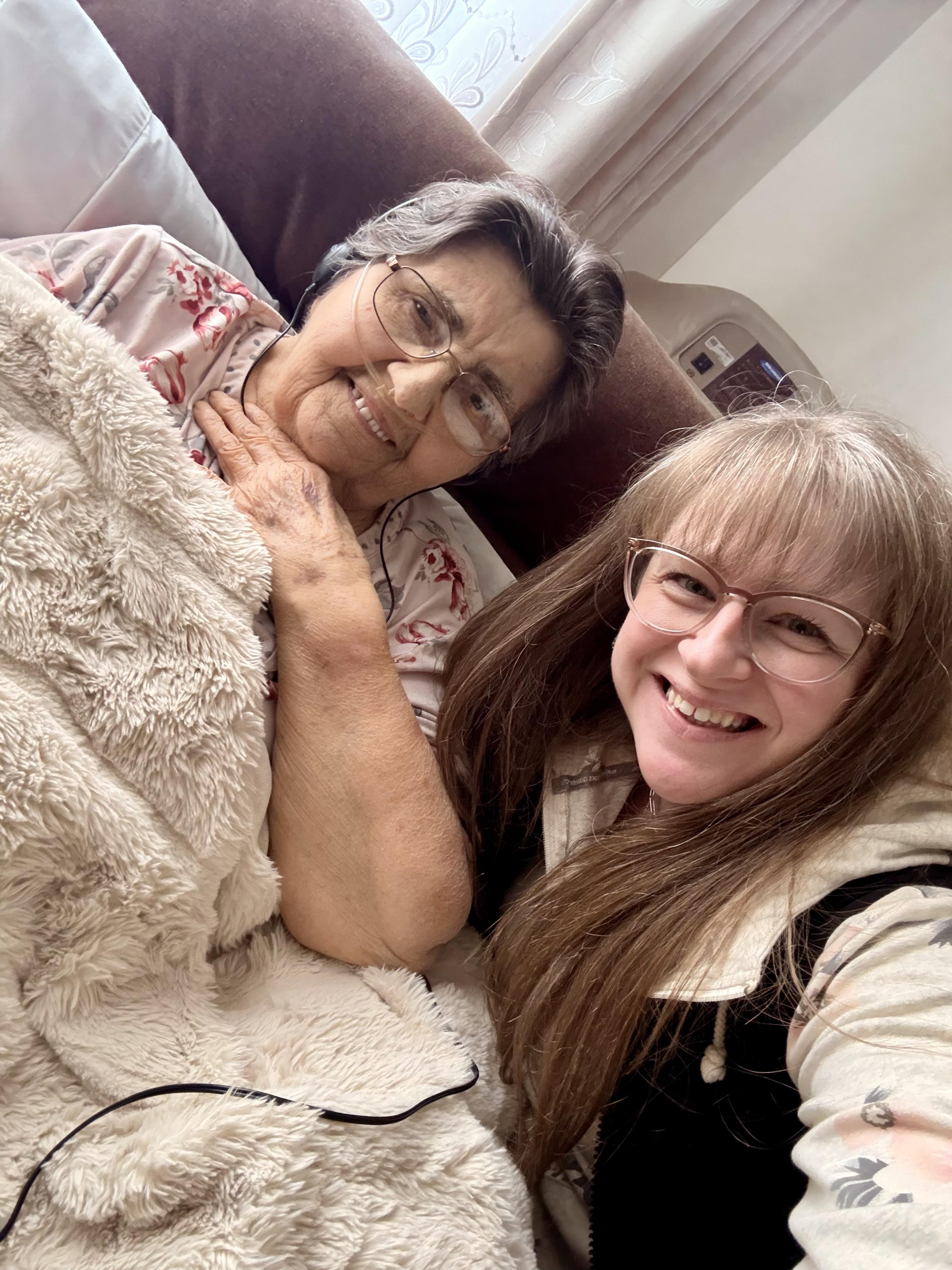 Two women smile together on a bed, sharing a joyful moment of connection.