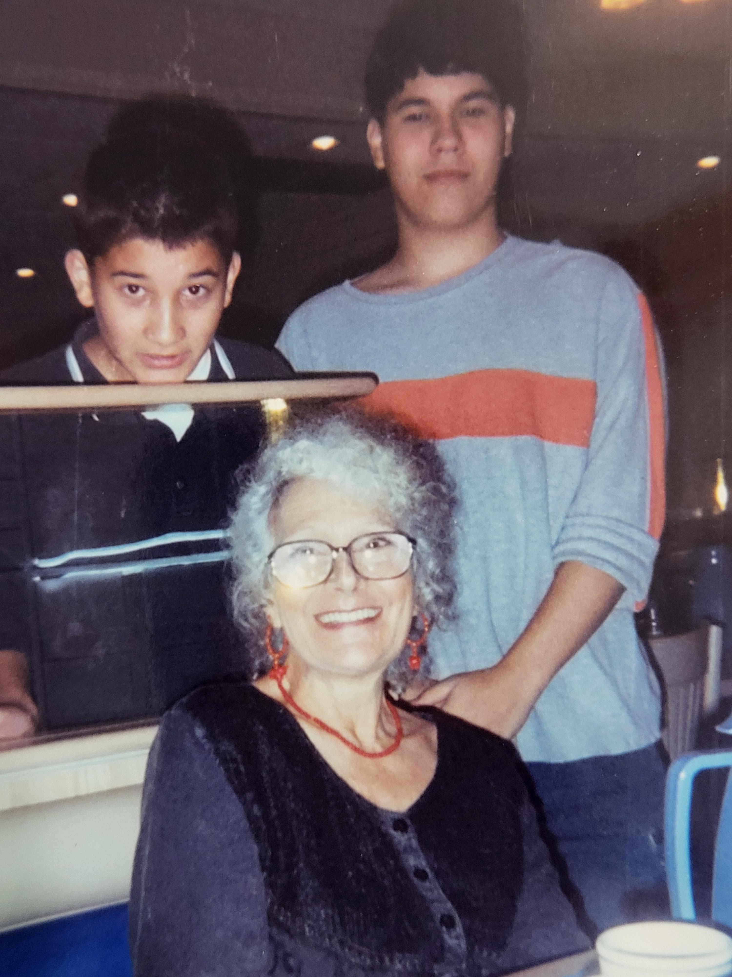 Two boys joyfully stand behind an elderly woman at a restaurant, sharing a moment together.