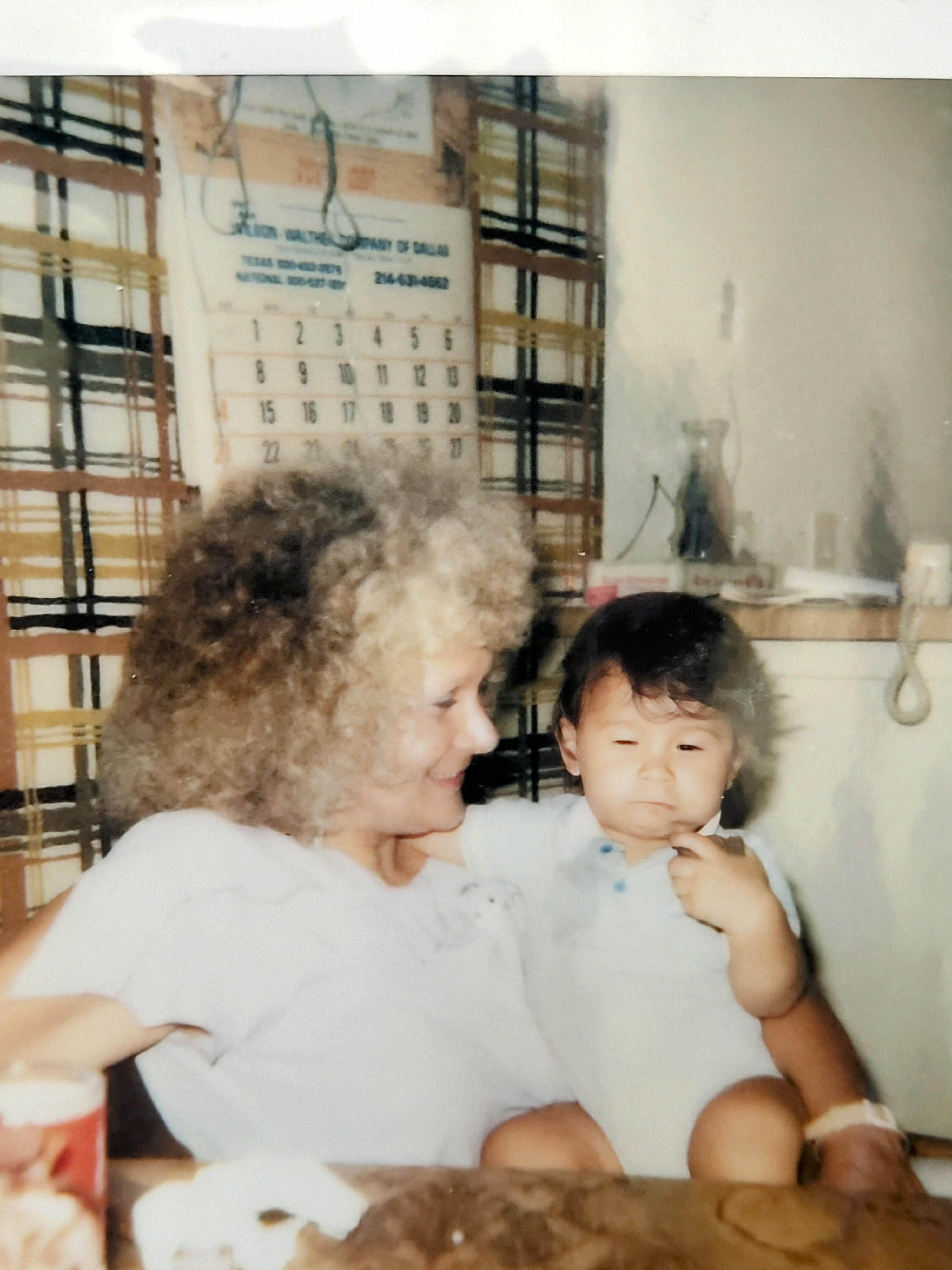 A smiling woman with curly hair enjoys a moment with a child indoors, creating warm memories.