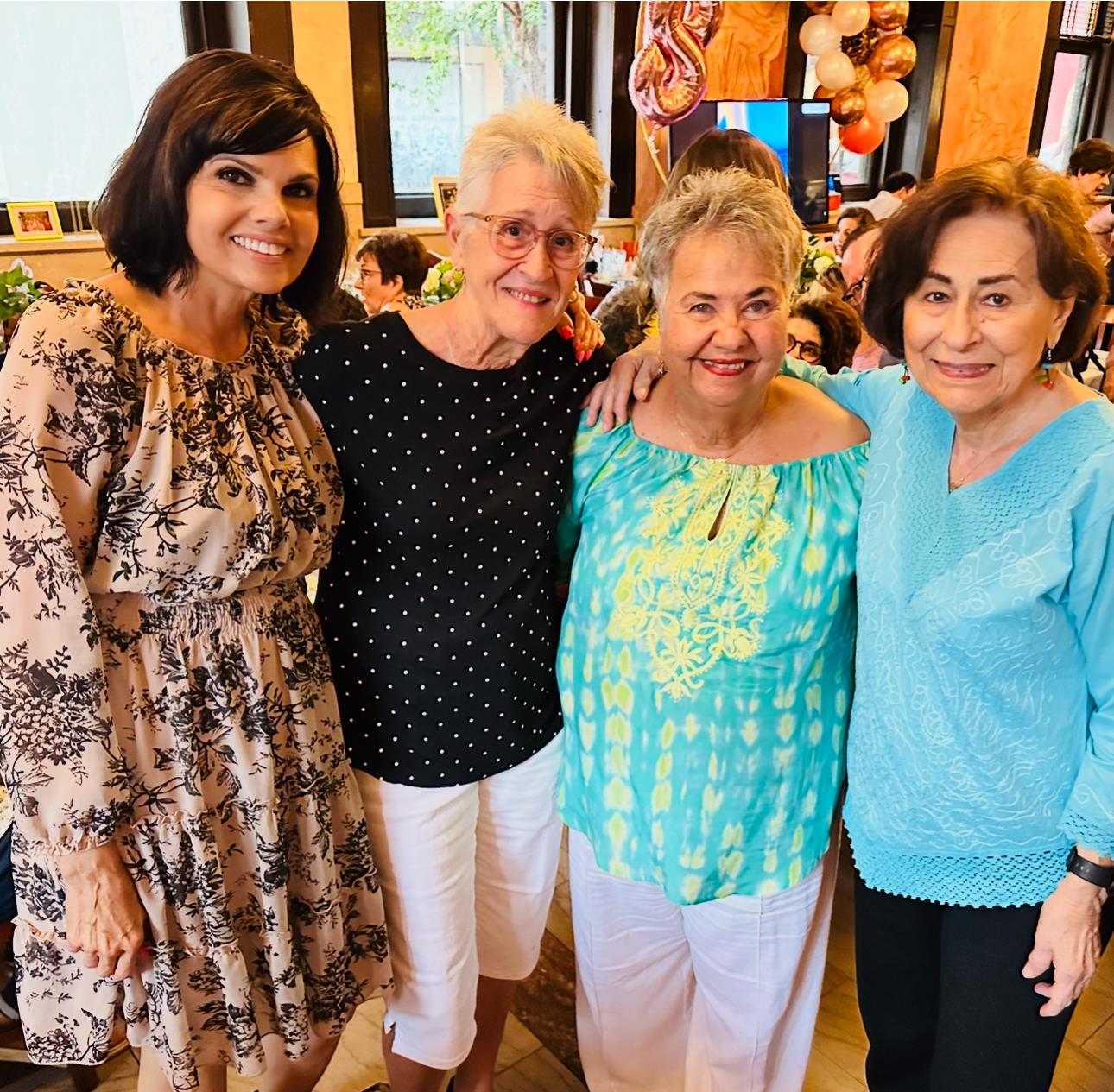 Four women smile together, enjoying a festive gathering full of laughter.