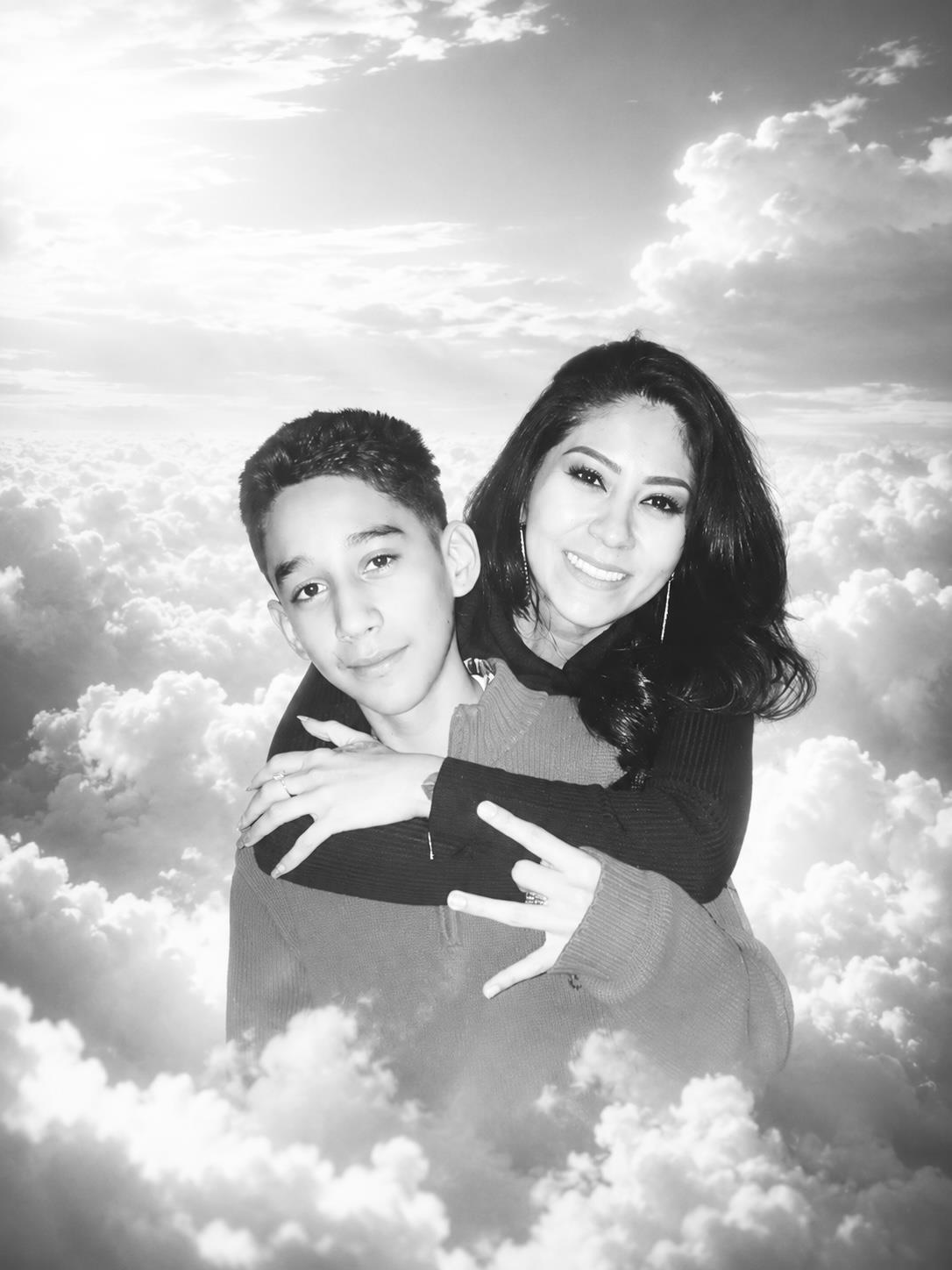 A woman hugging a boy in front of clouds