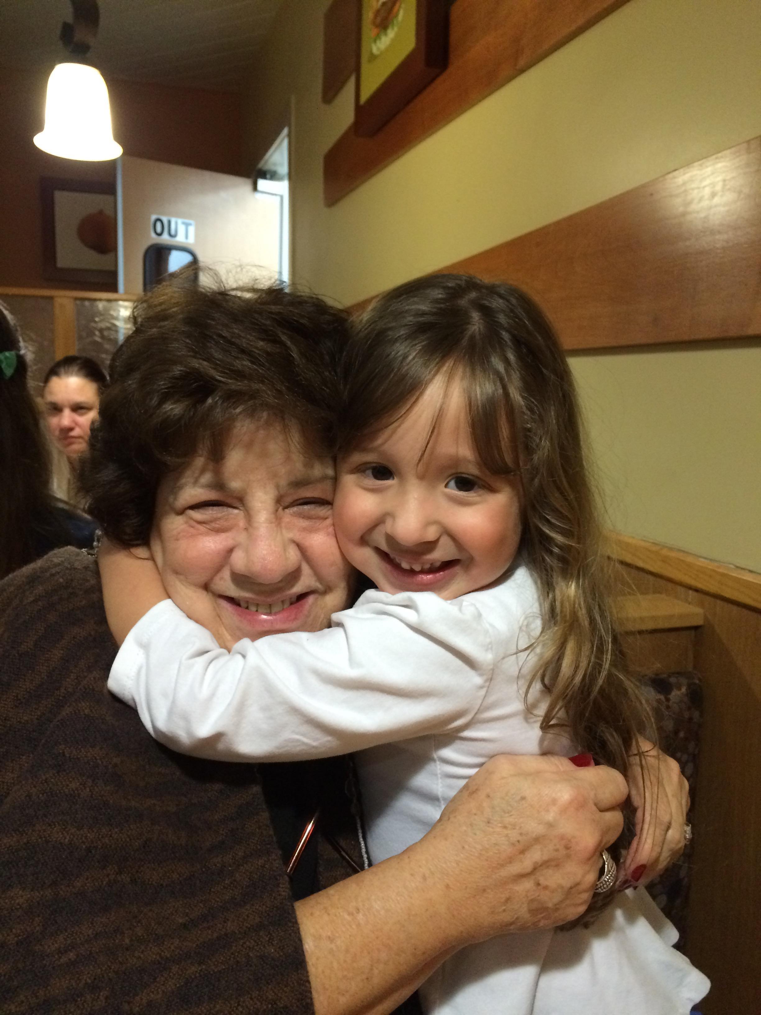 A lively interaction unfolds as a grandmother joyfully hugs her granddaughter in a warm cafe.