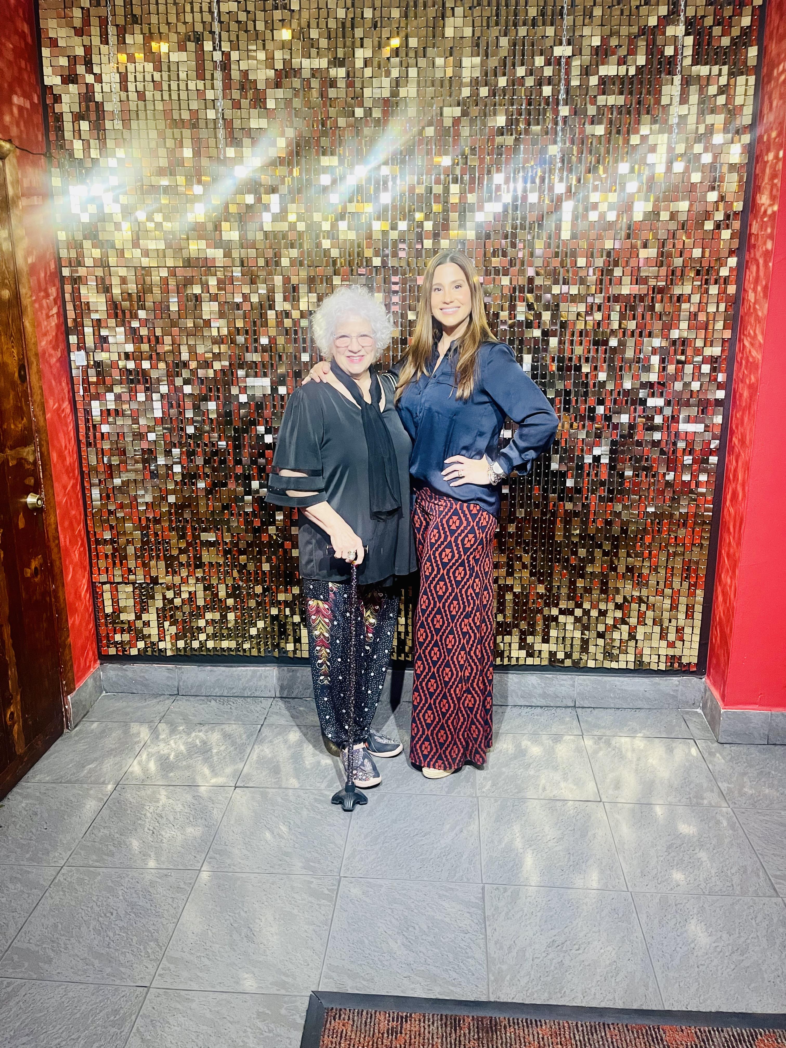 Two women stand side by side, smiling in front of a dazzling backdrop, enjoying a joyful evening.