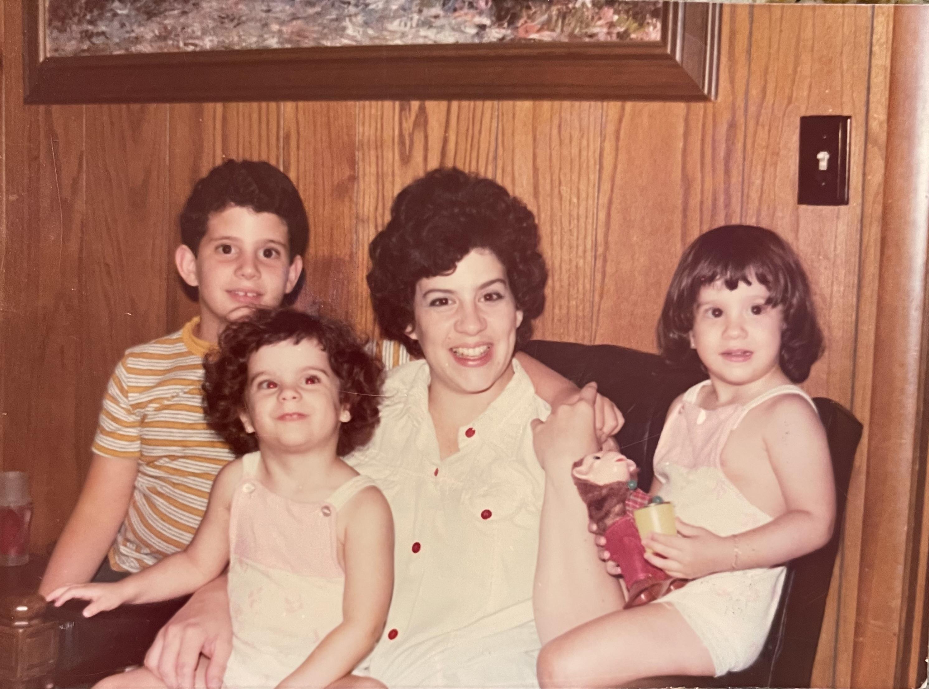Children are joyfully gathered around a woman in a welcoming living room setting.