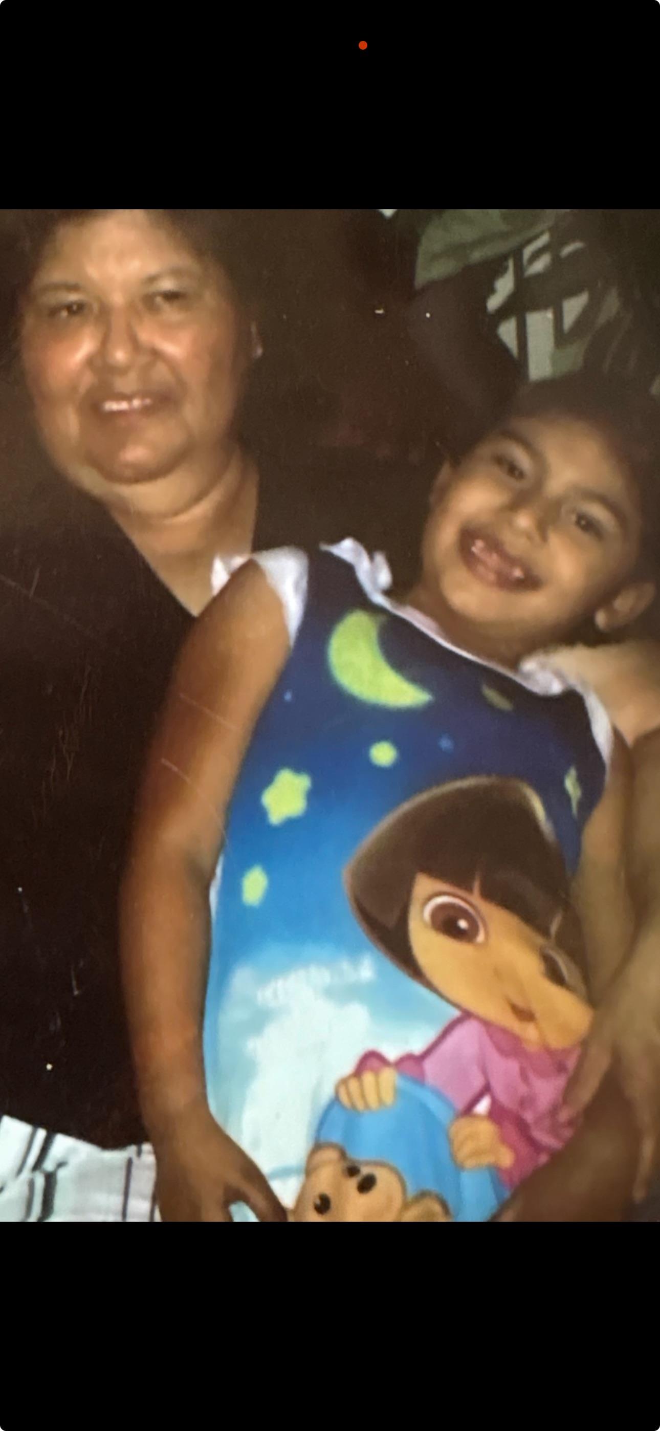 A happy young girl wearing a colorful shirt enjoys a moment with her smiling grandmother.