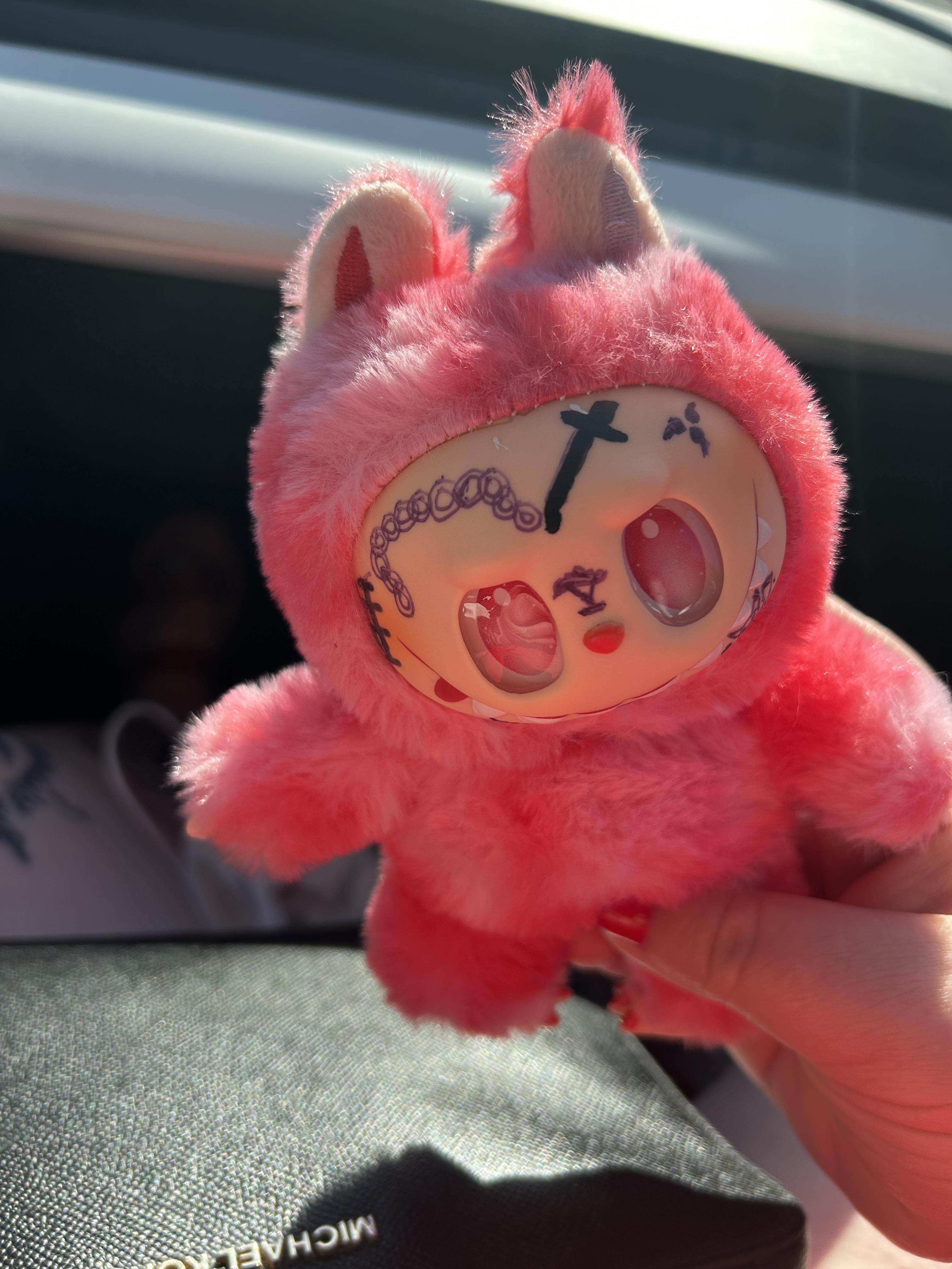 A soft pink plush toy with a unique face is being held outside, showing its playful details.