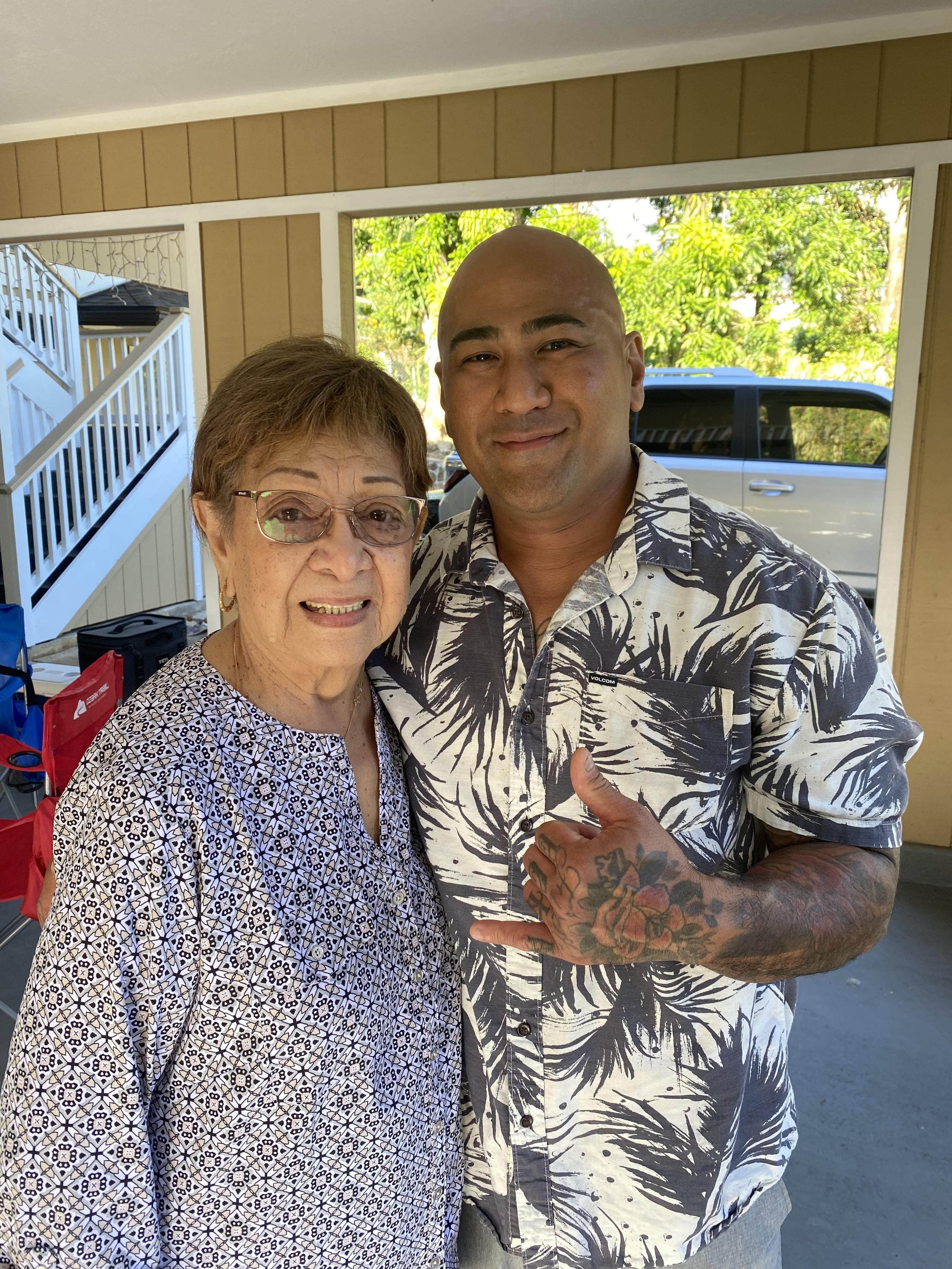 A grandmother and her grandson are smiling together outdoors, capturing a joyful family moment.