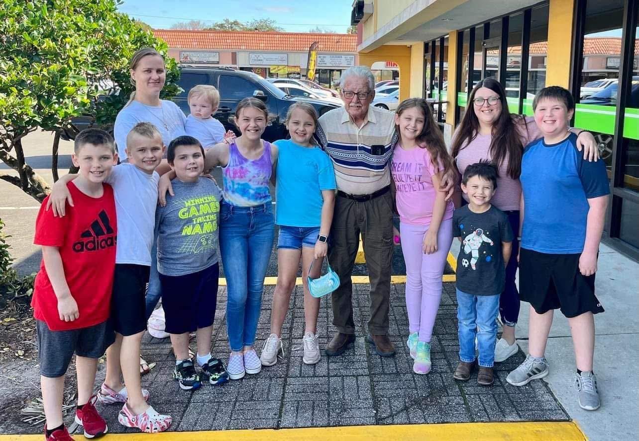 A group of children and adults happily gather outside a shop, sharing a joyful moment.