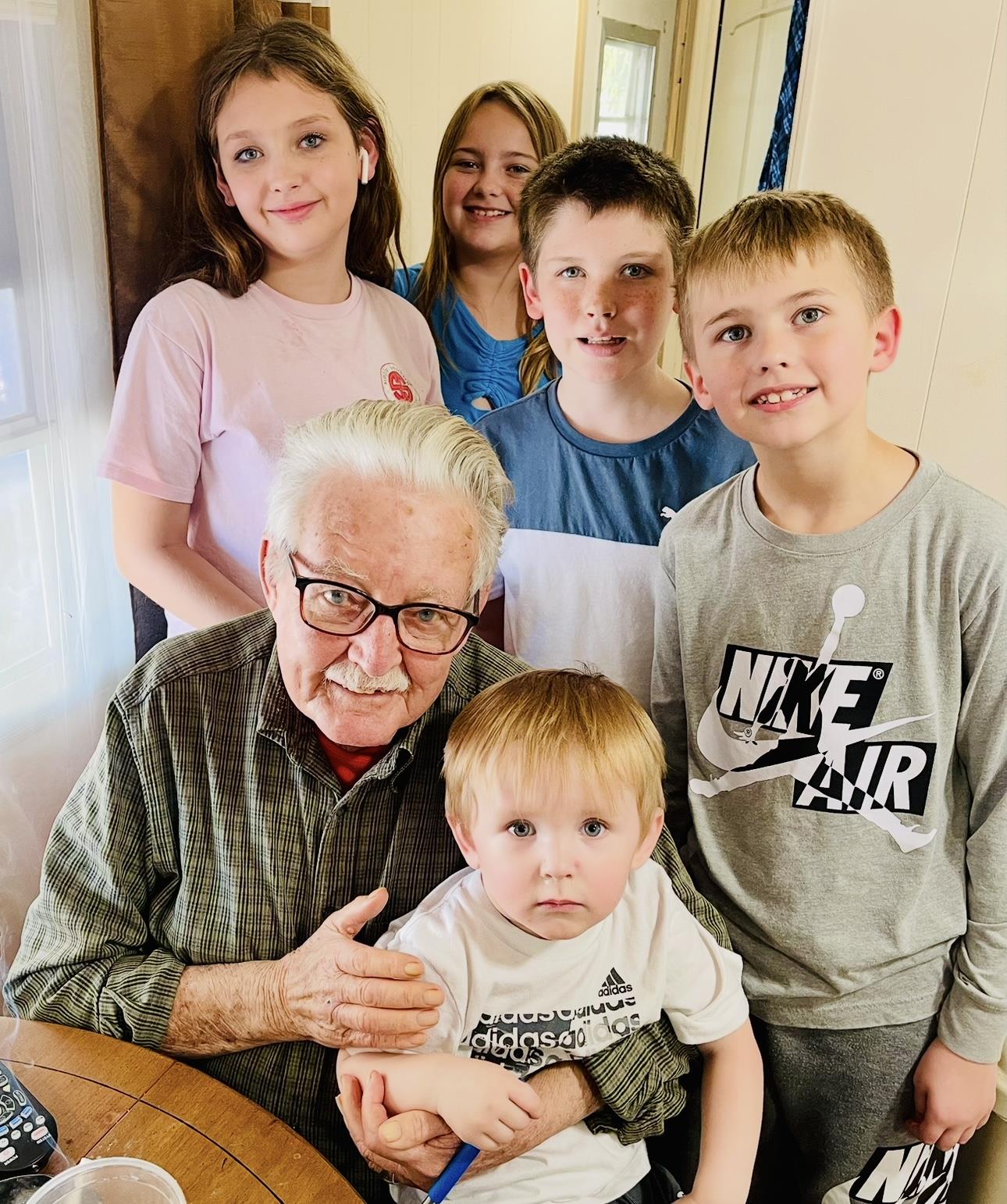 Children surround an elderly man, smiling and enjoying quality time together in a warm atmosphere.