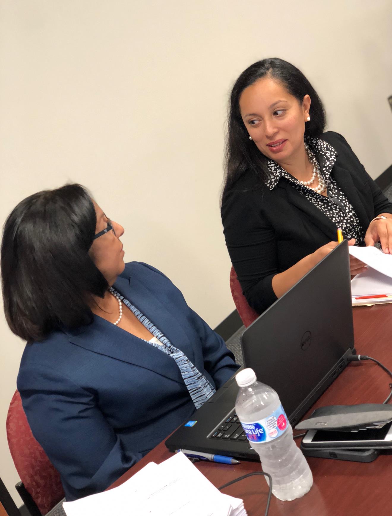 Two women engaged in a discussion, sharing ideas at a conference table during a meeting.