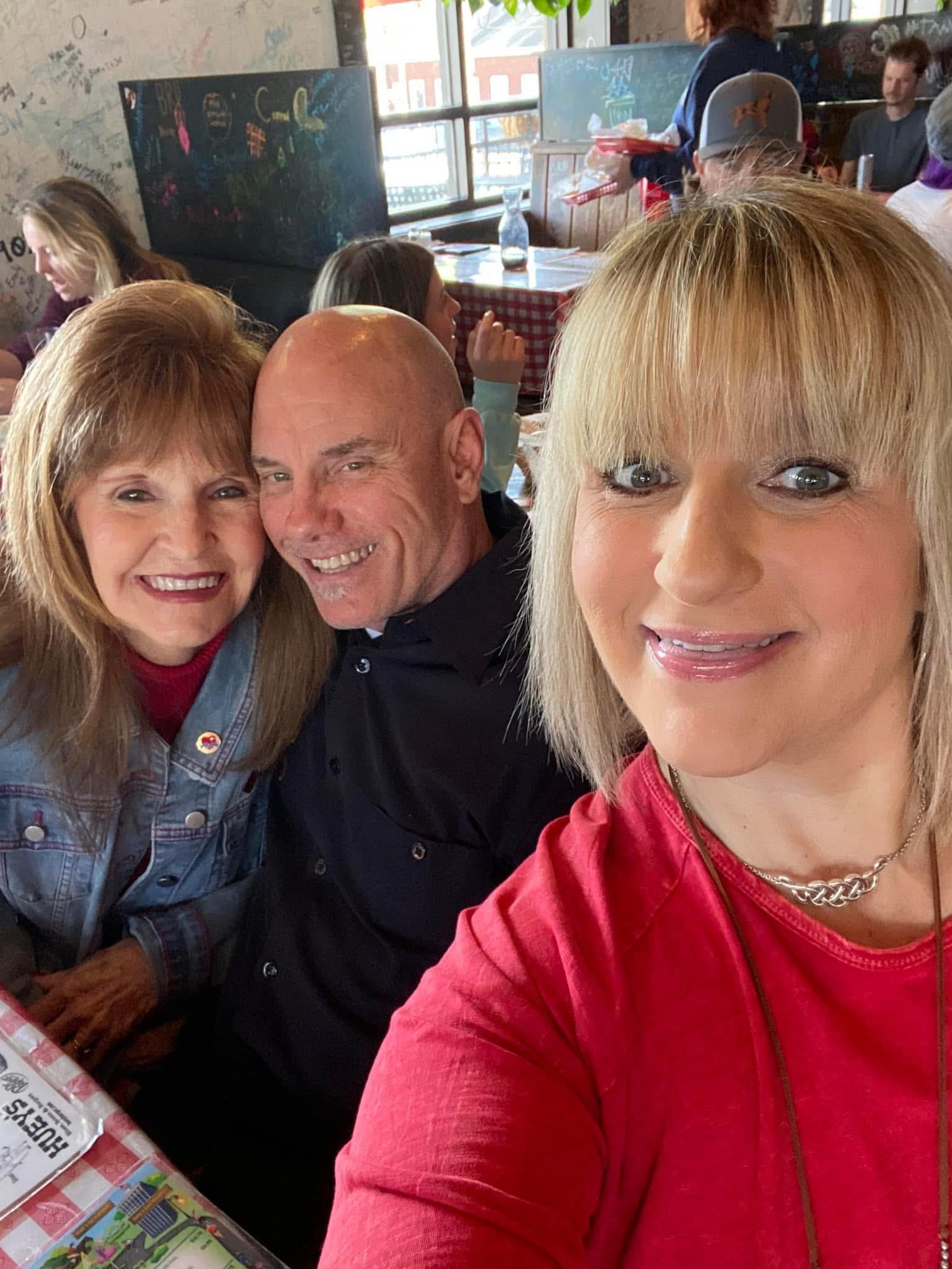 Three friends smile widely while sharing a joyful moment at a vibrant lunch spot.