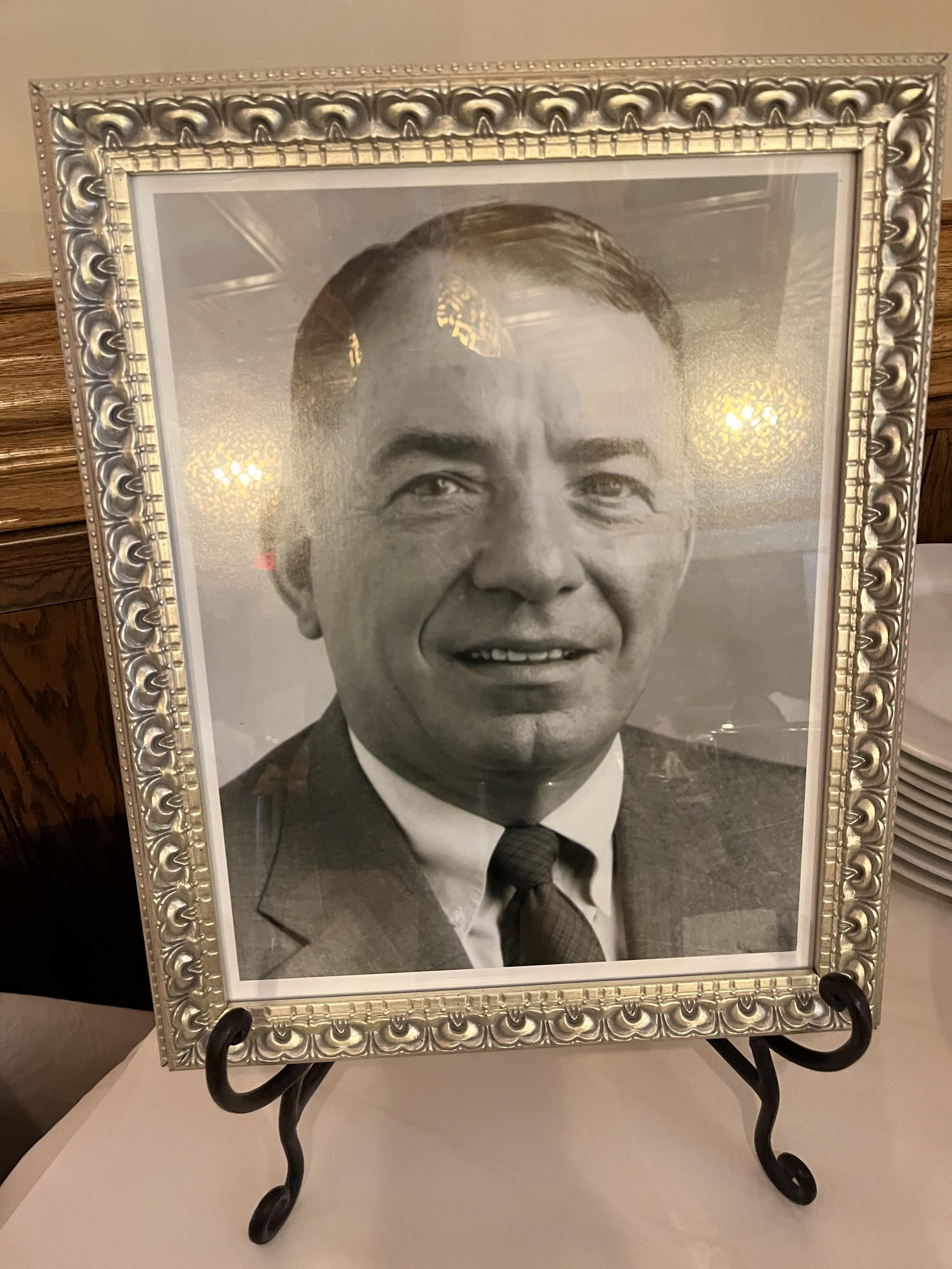 A smiling man in a suit captured in black and white, framed elegantly on a table.