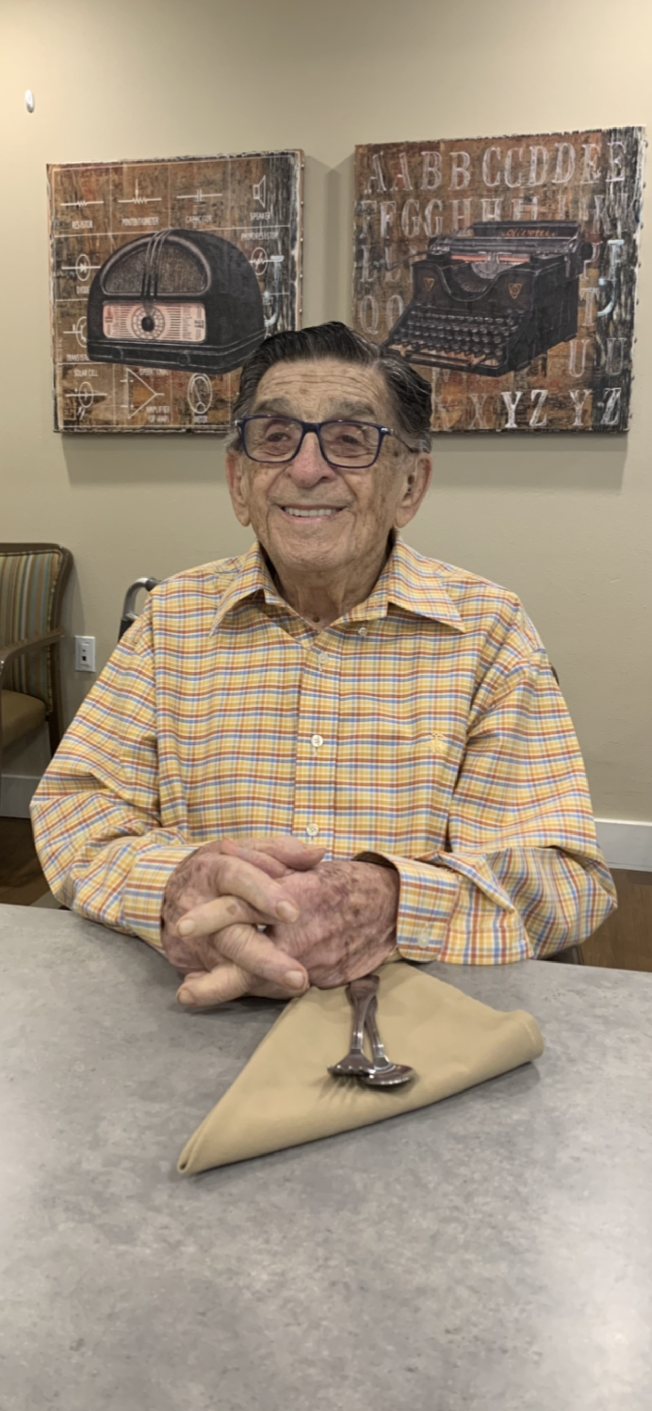 An elderly man is smiling warmly while sitting at a table in a community center.