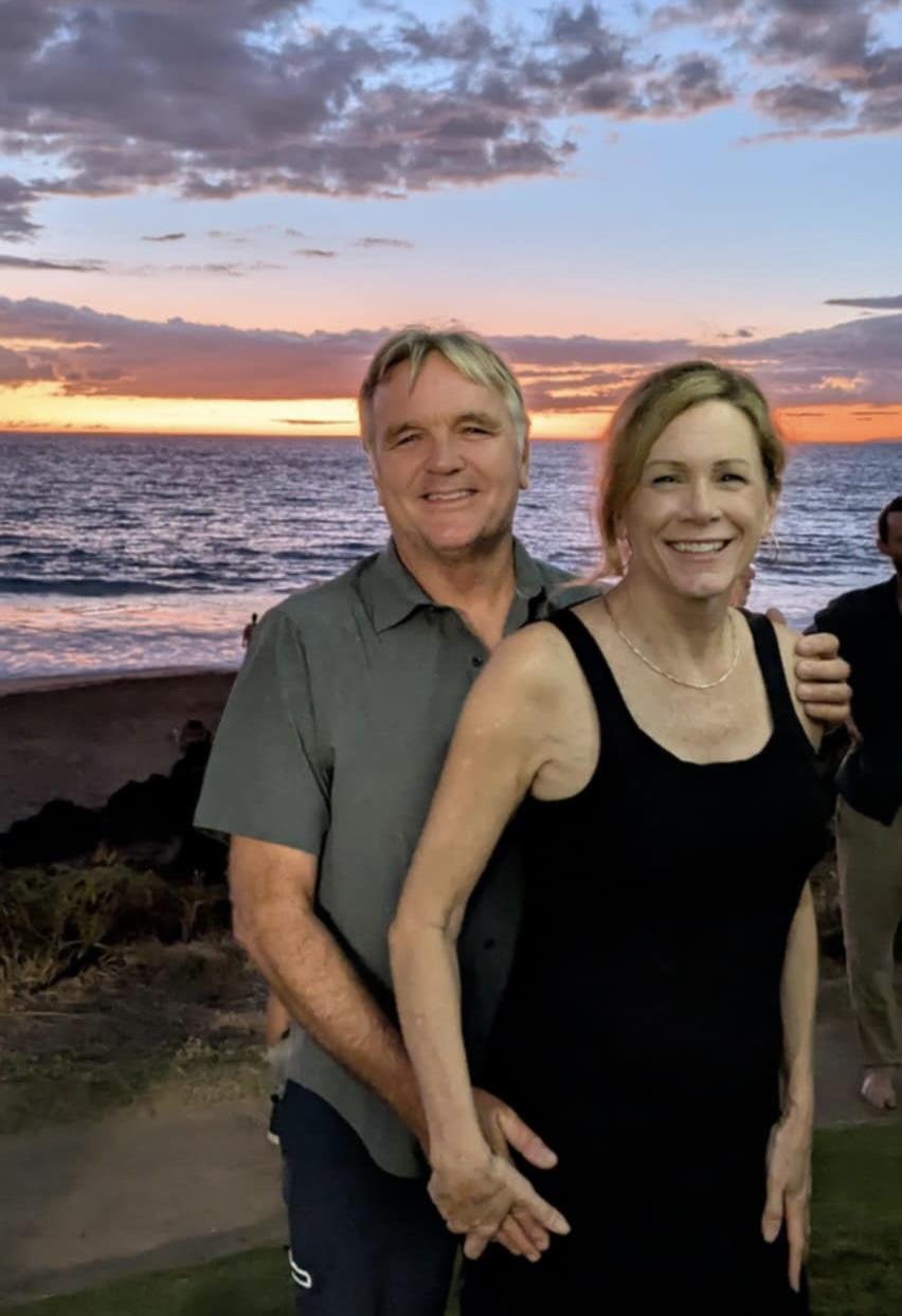 Happy couple poses together on the beach, surrounded by friends during a stunning sunset.