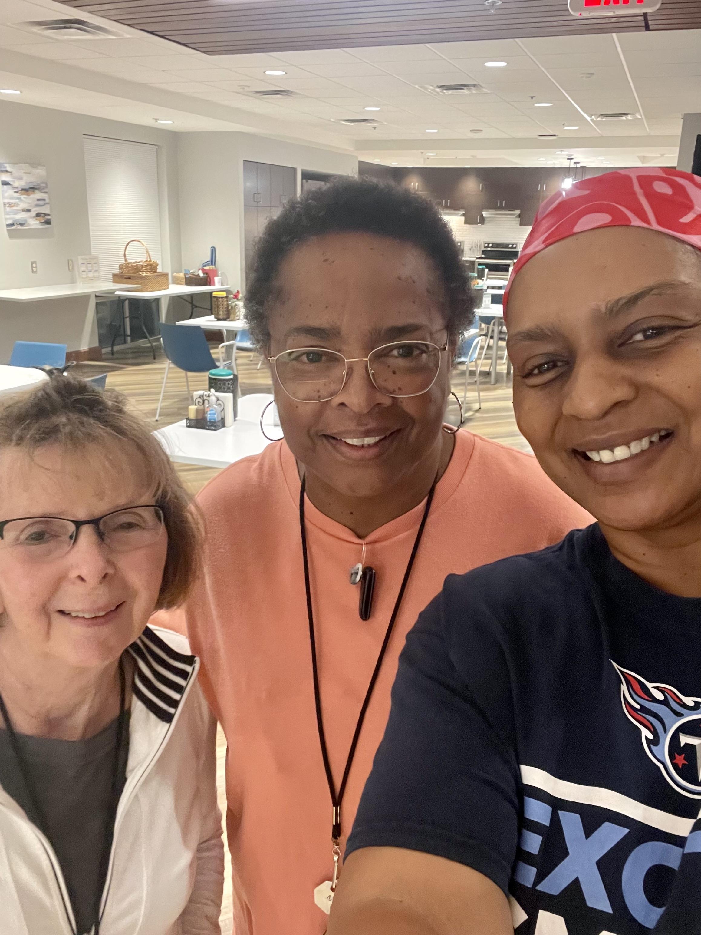 Three friends smile together in a community center, celebrating their companionship and connection.
