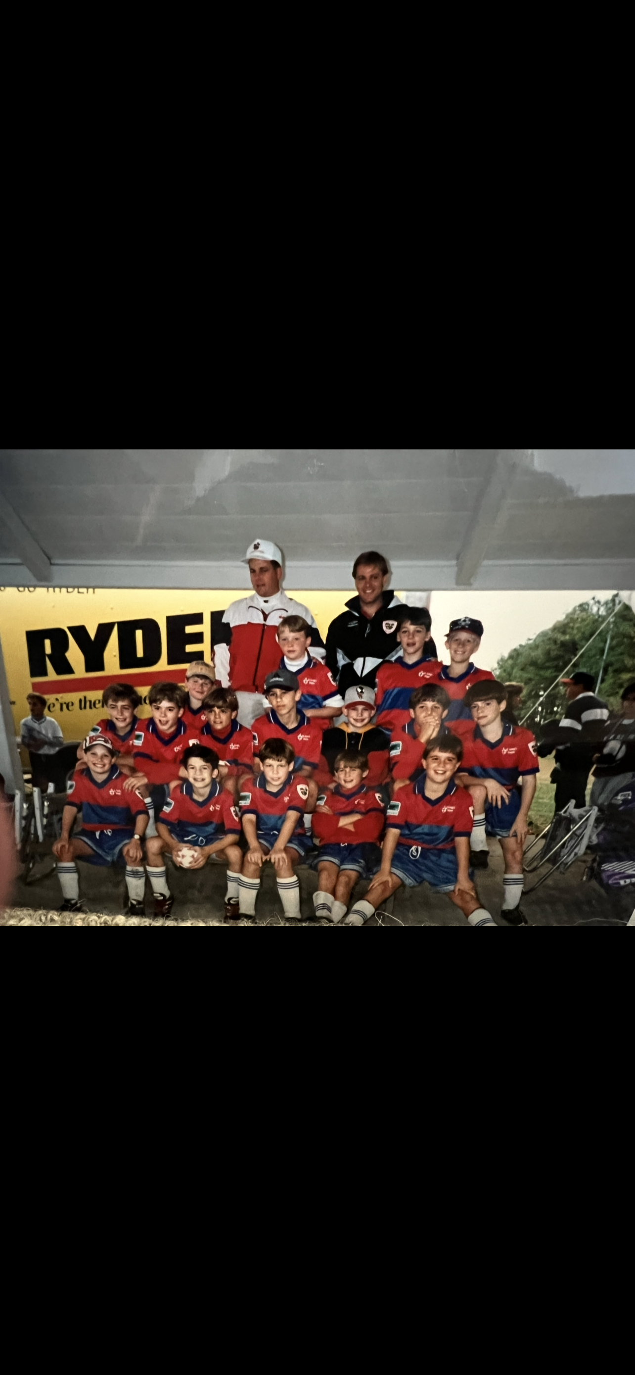 A youth soccer team gathers for a group photo with their coach after a match on a sunny day.