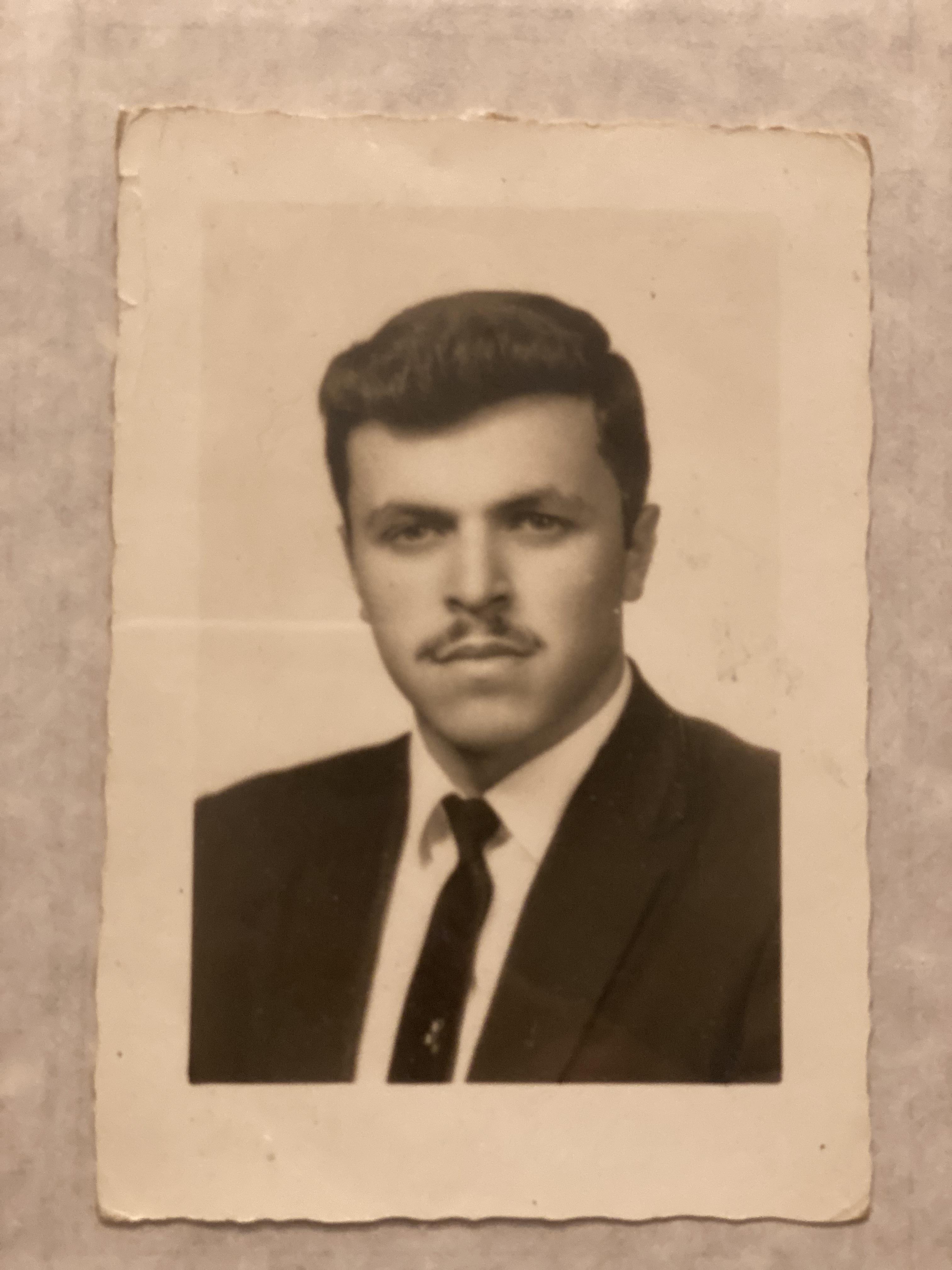 A young man poses confidently in formal attire, showcasing a distinguished moustache and hairstyle.