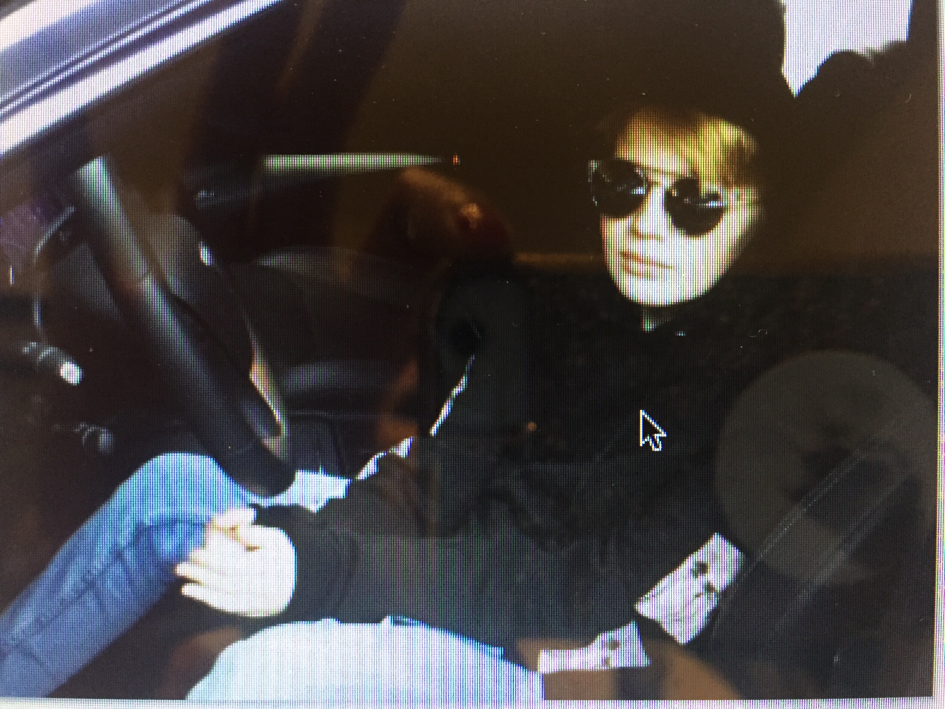 Individual in a black hoodie and sunglasses relaxed inside a parked car on a street.