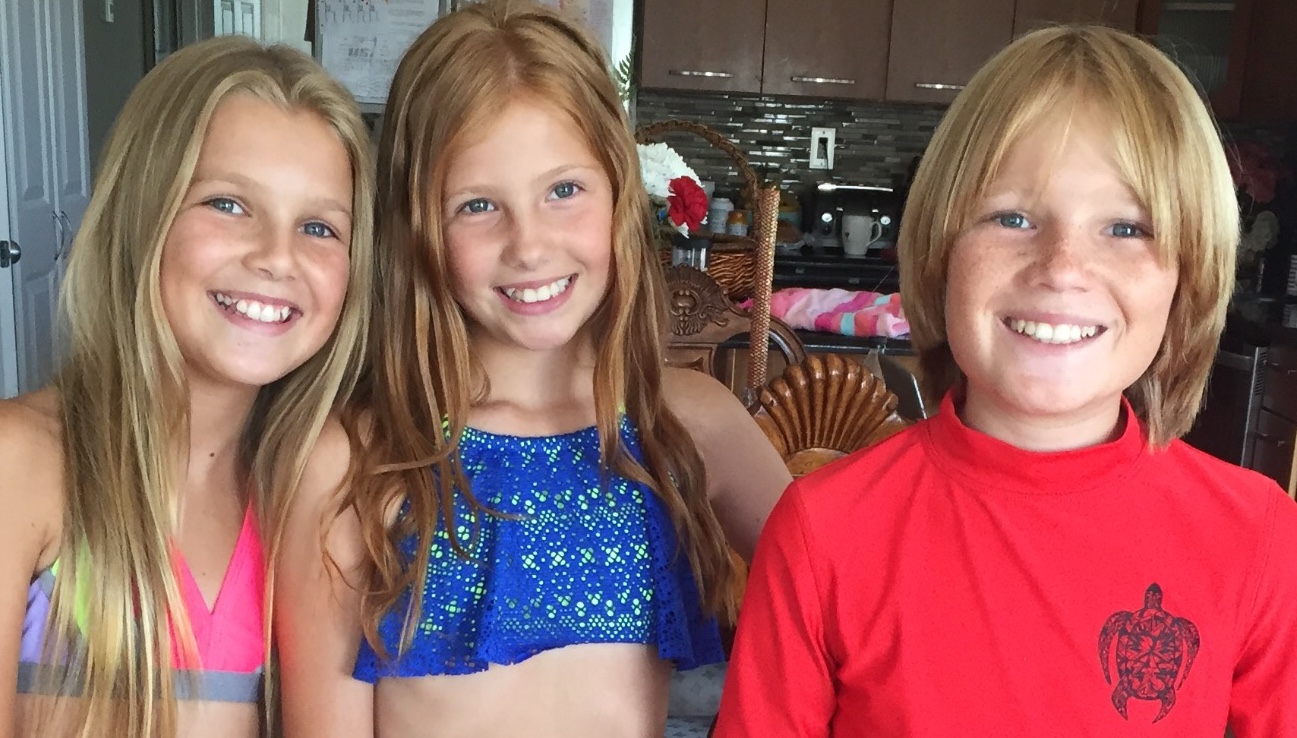 Three smiling children pose together indoors, showcasing their colorful swimwear and happiness.