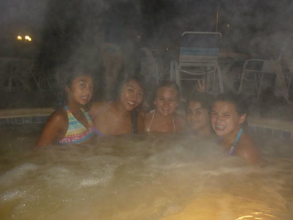 Group of friends laughing and relaxing in a hot tub under the night sky.