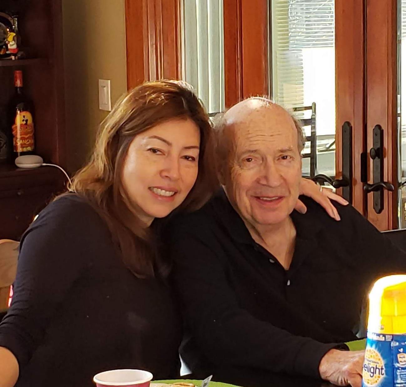 Two relatives are happily posing for a photo in a well-lit kitchen.