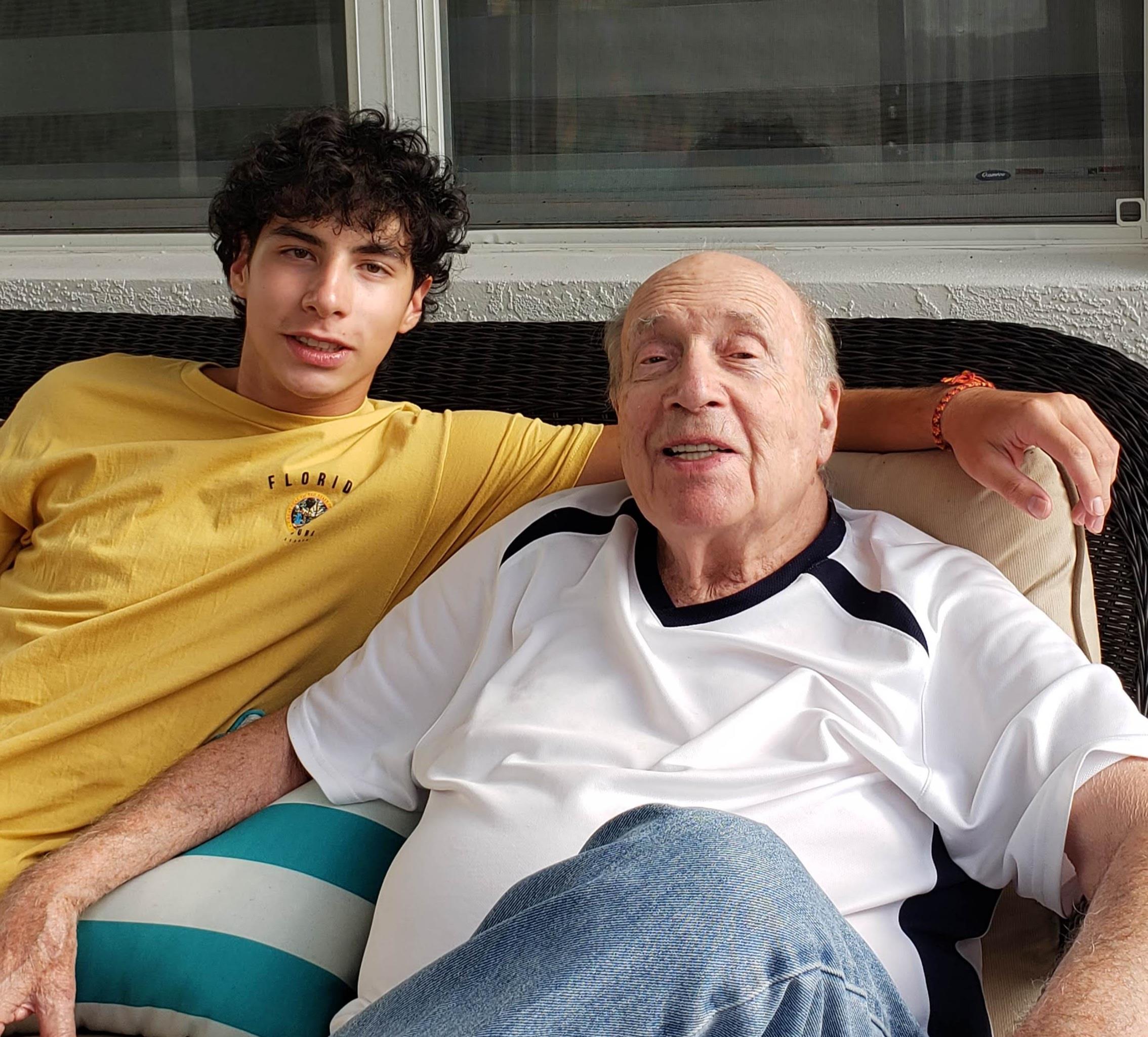 Young man and older man sit together on a comfortable couch, smiling and enjoying their time.