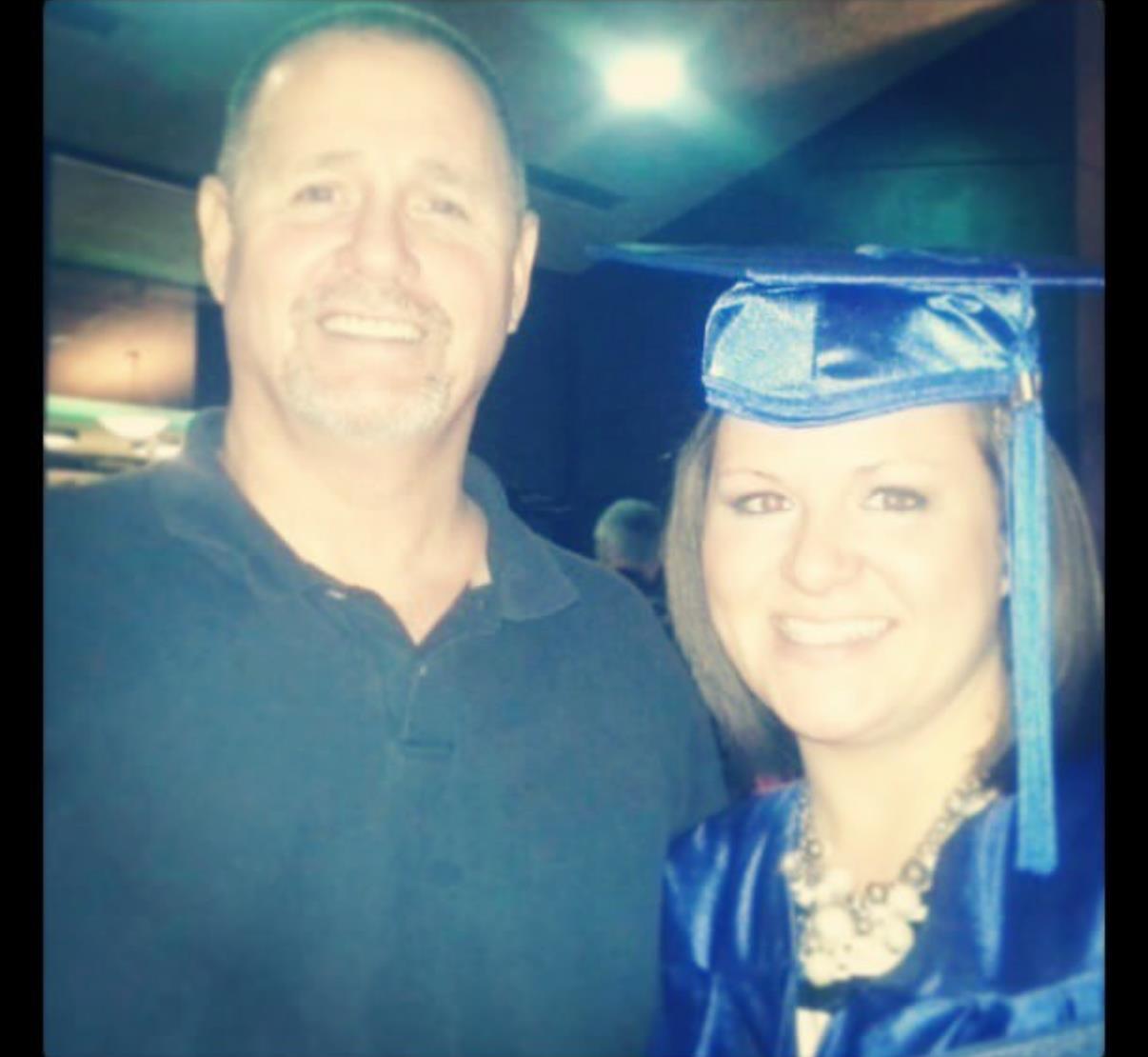 A proud graduate smiles next to a supporter, both celebrating a significant achievement together.