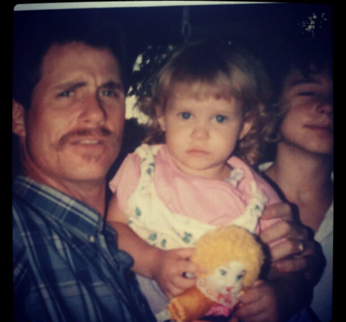 A father embraces his young daughter while siblings smile in the background at a family gathering.