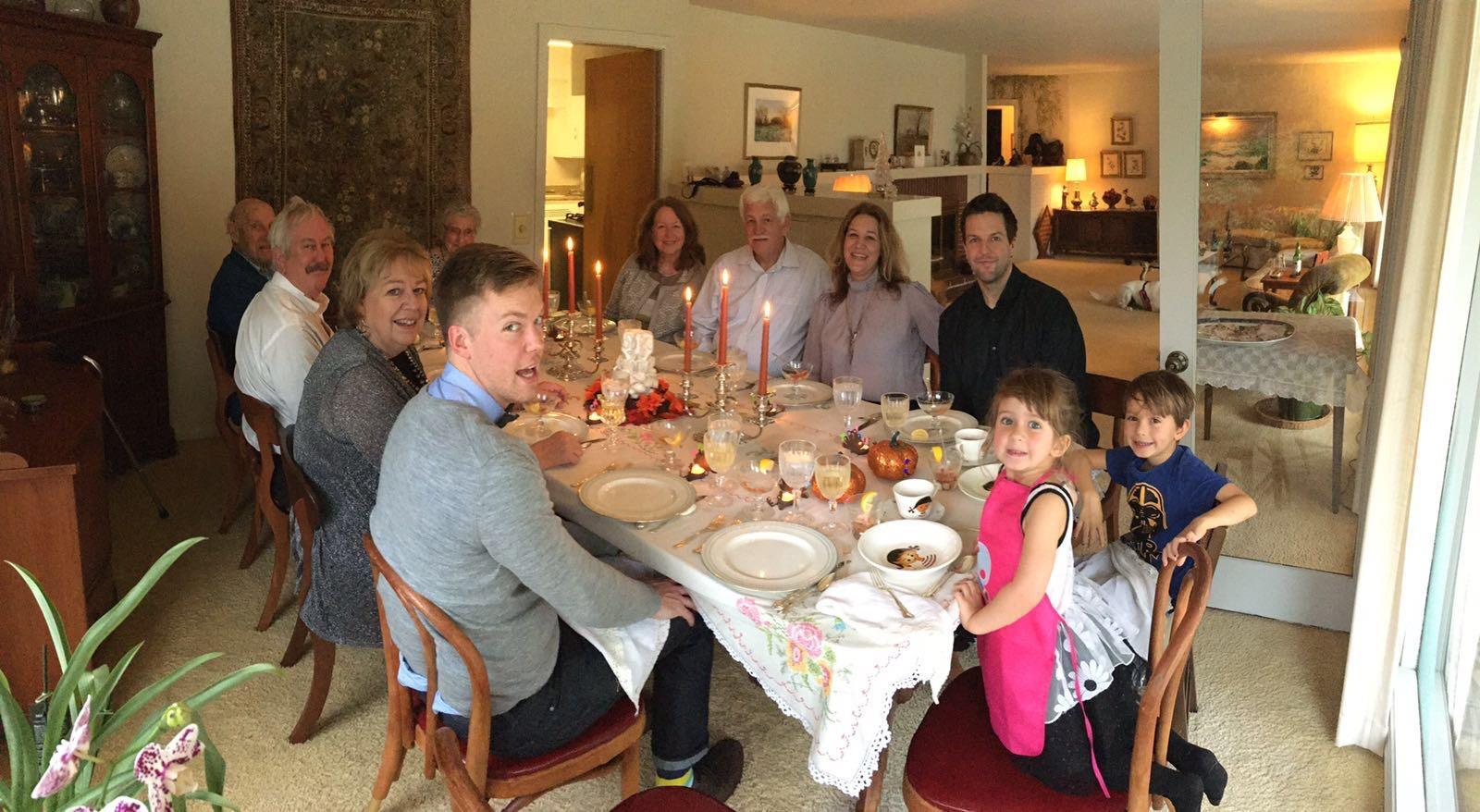 Family members enjoy a cheerful gathering around a dinner table decorated with dishes and candles.