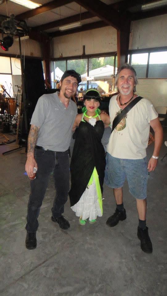 Three people joyfully pose at a vibrant festival, flaunting their unique styles.