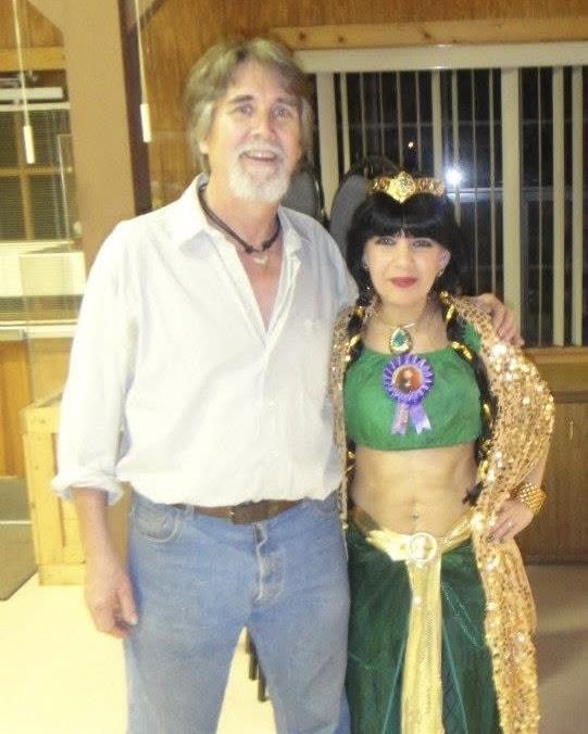 Two individuals pose together wearing vibrant costumes, celebrating at an indoor event.