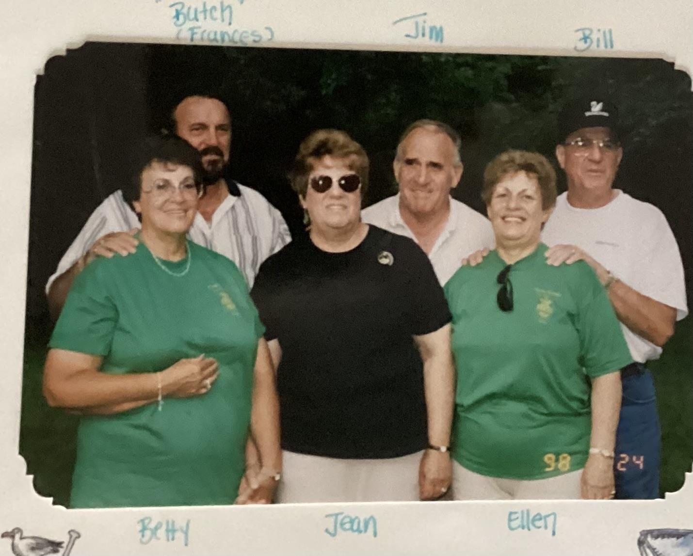 Several friends pose together wearing matching shirts, enjoying a sunny day at the park.
