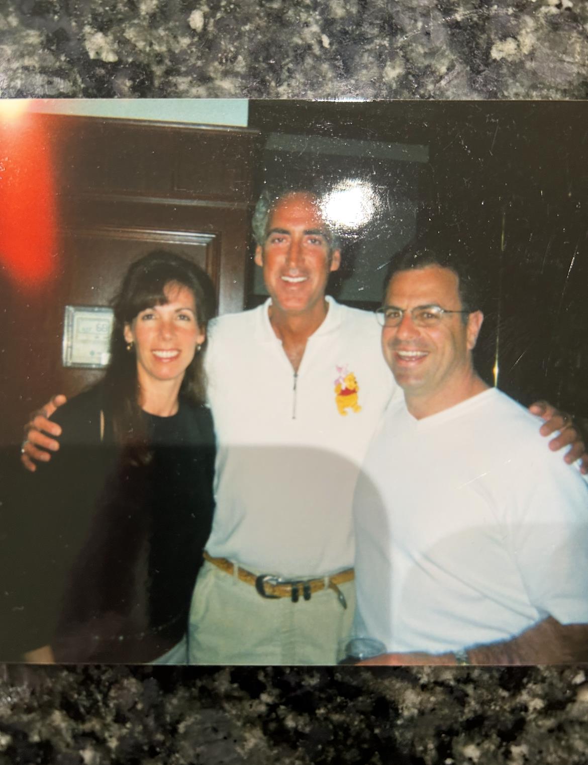 Three friends are smiling and posing together, enjoying their time at a social event indoors.