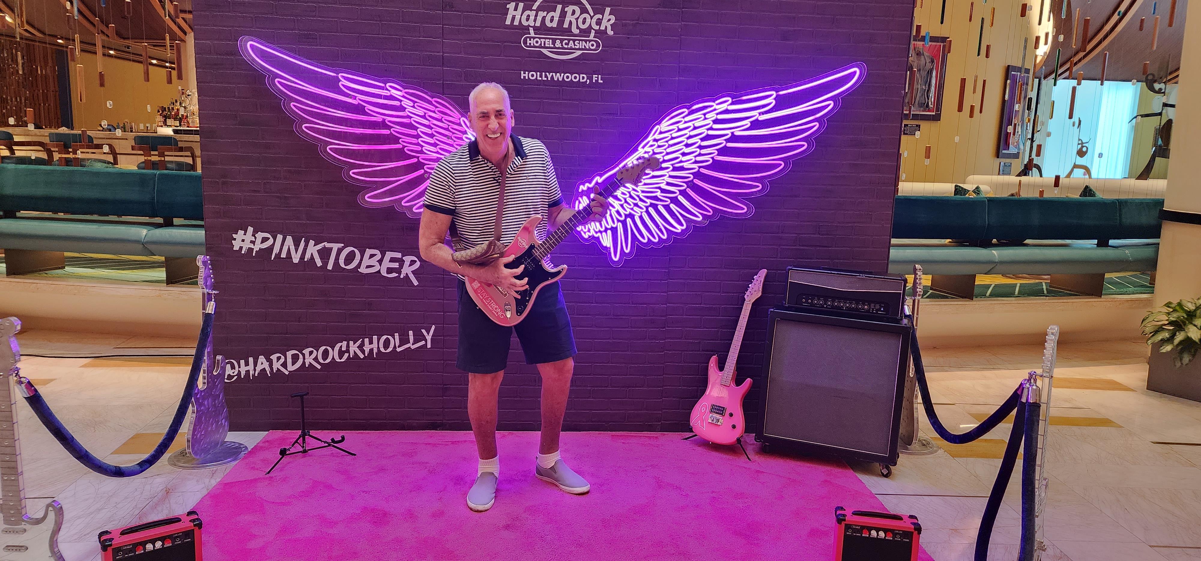 A man enjoys playing an electric guitar against a colorful neon backdrop in Hollywood.