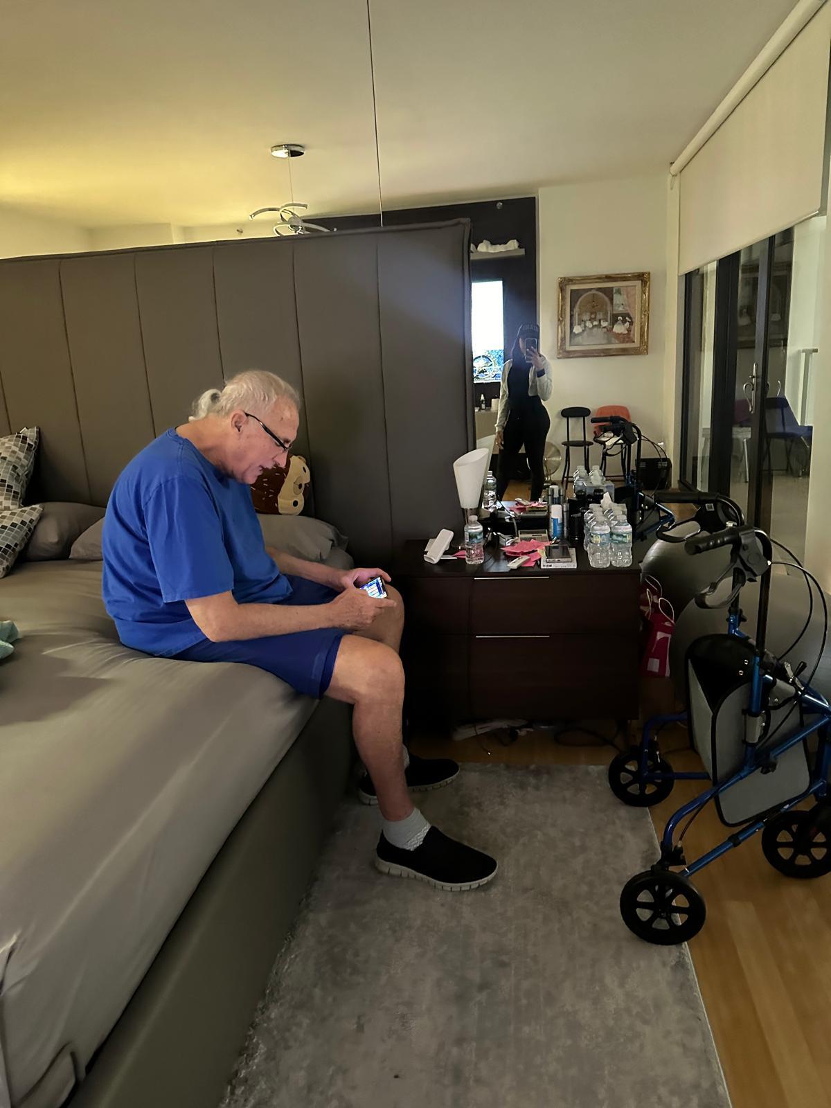 Senior man engages with a mobile device while seated on a bed in a cozy bedroom setting.