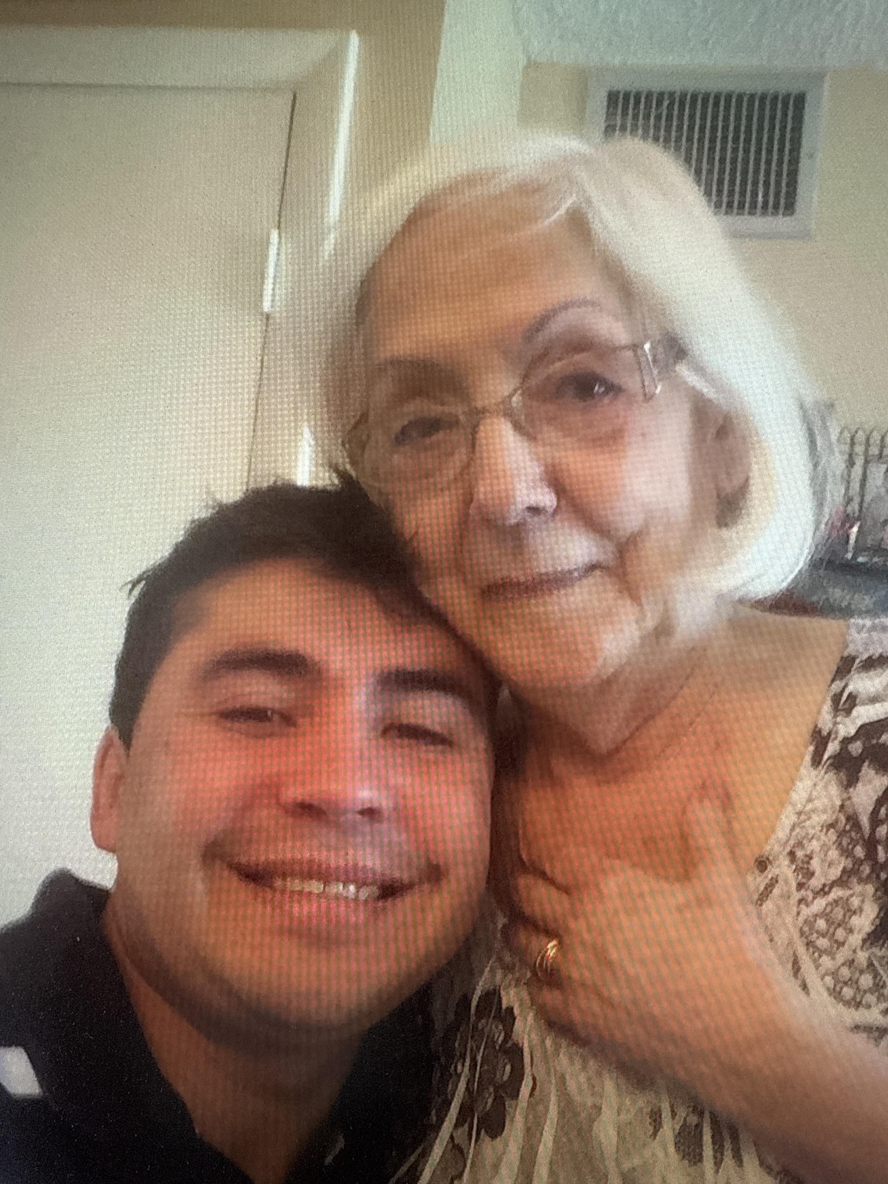 A young man and an elderly woman smile warmly together in a cozy setting.