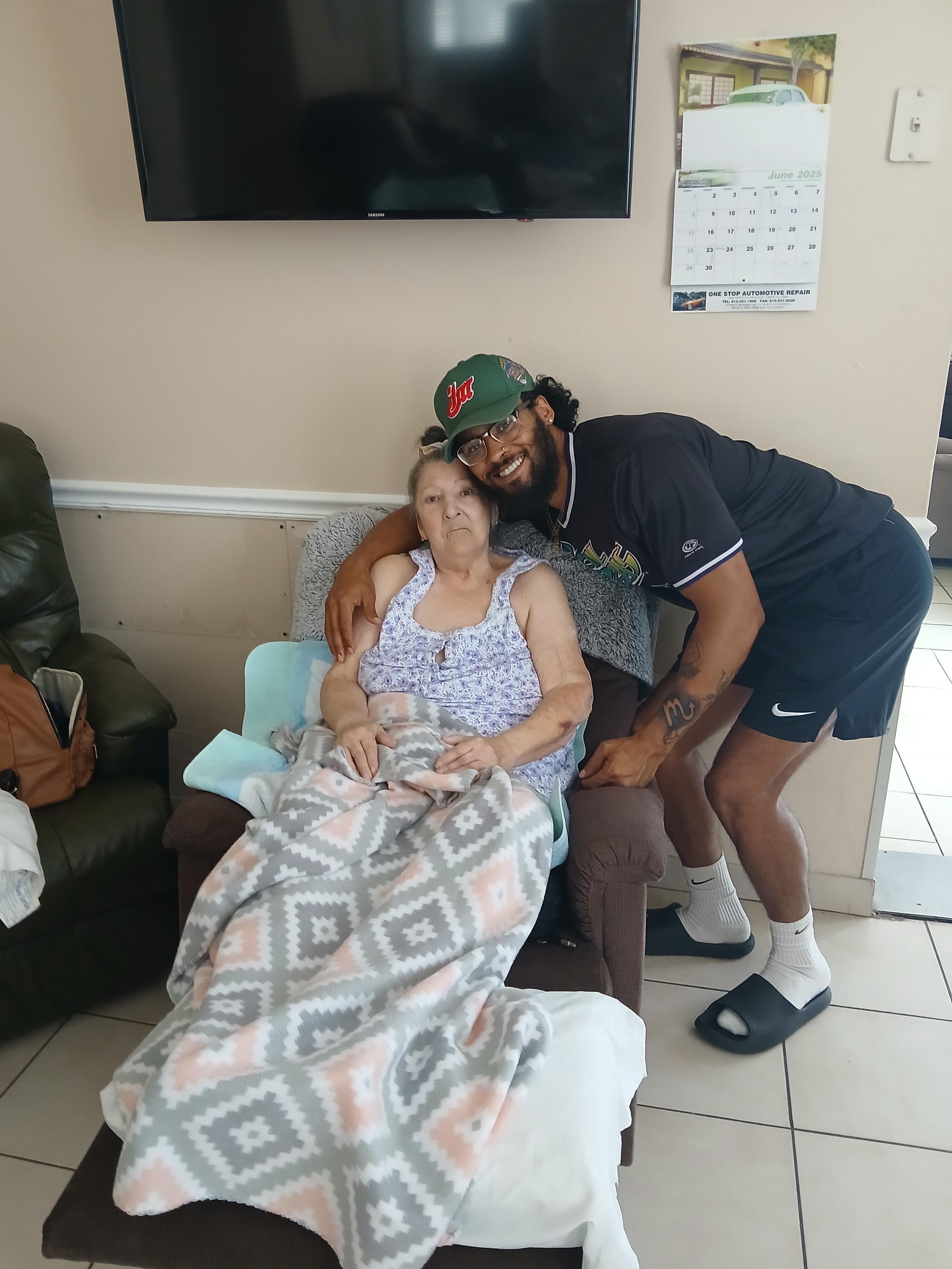 A young man shares a joyful hug with an older woman while seated comfortably in a living room.