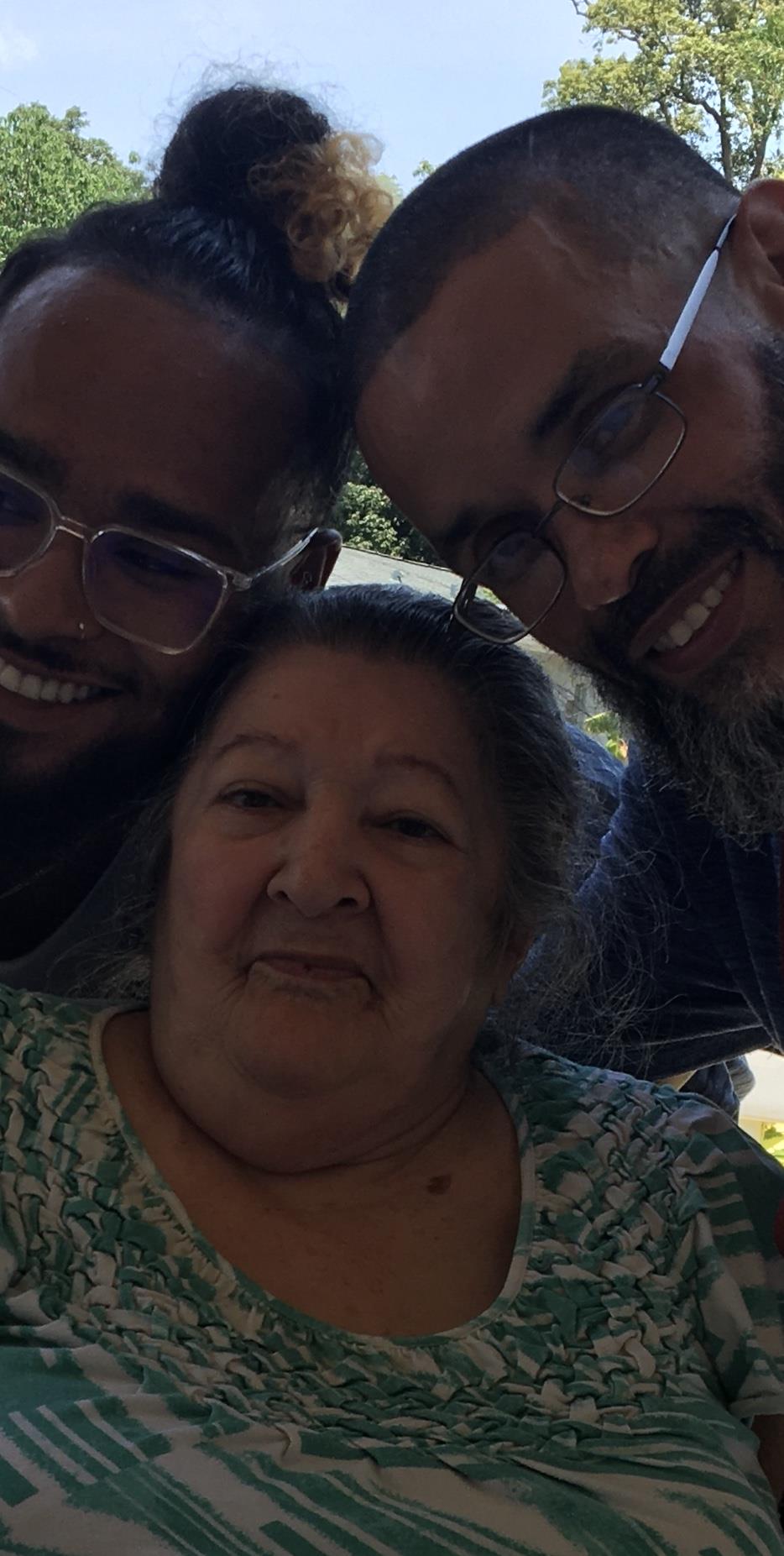 Three family members smile together outdoors, enjoying a joyful moment in nature.