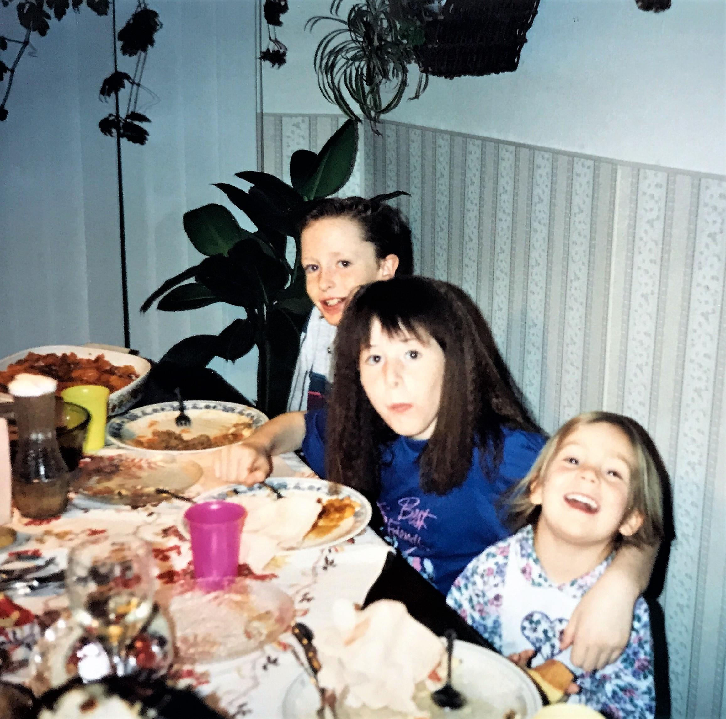 Three children share joyful moments at a table filled with delicious food and decorations.
