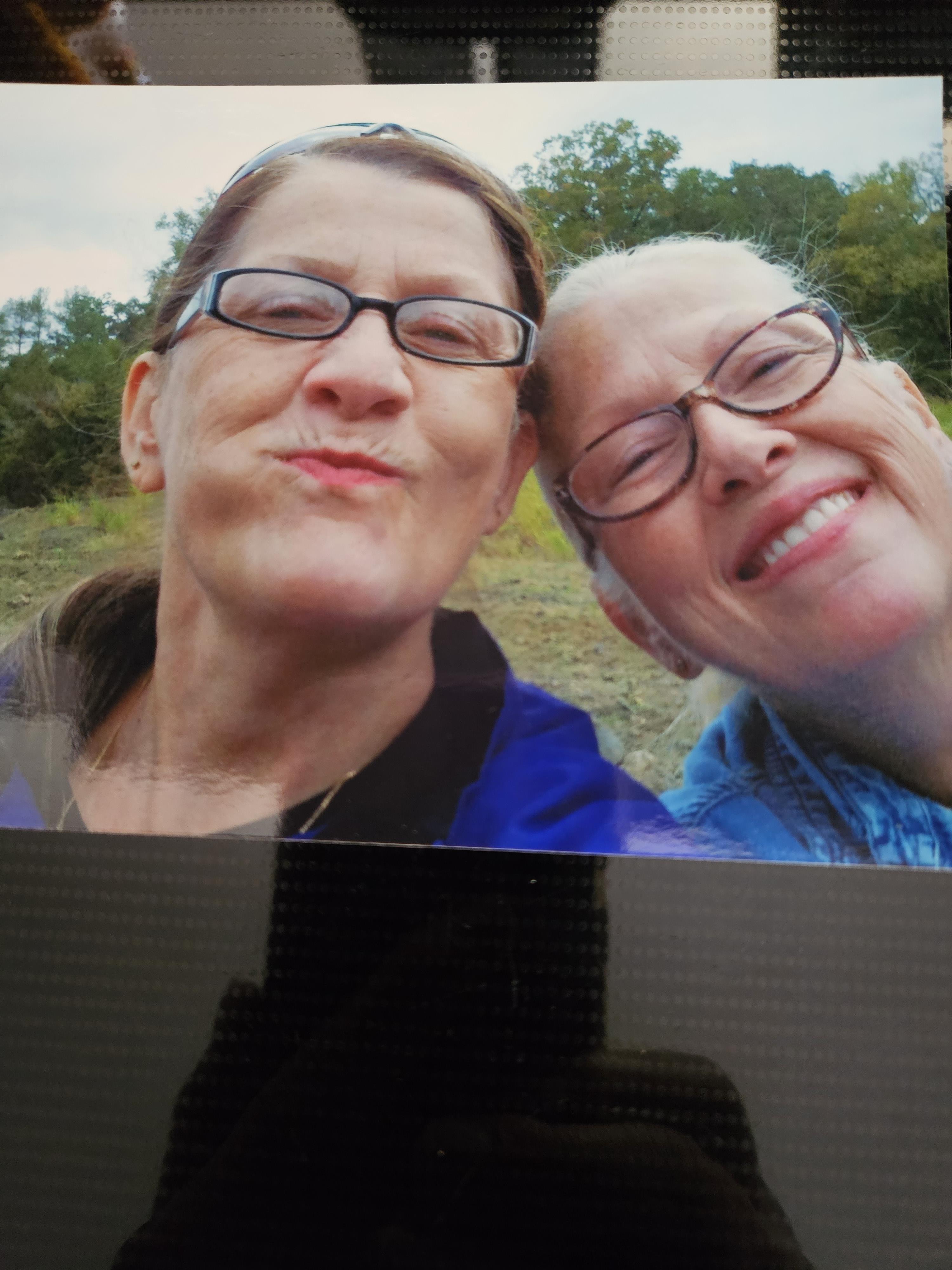 Two friends smile happily at the camera while sitting outside in a natural setting.