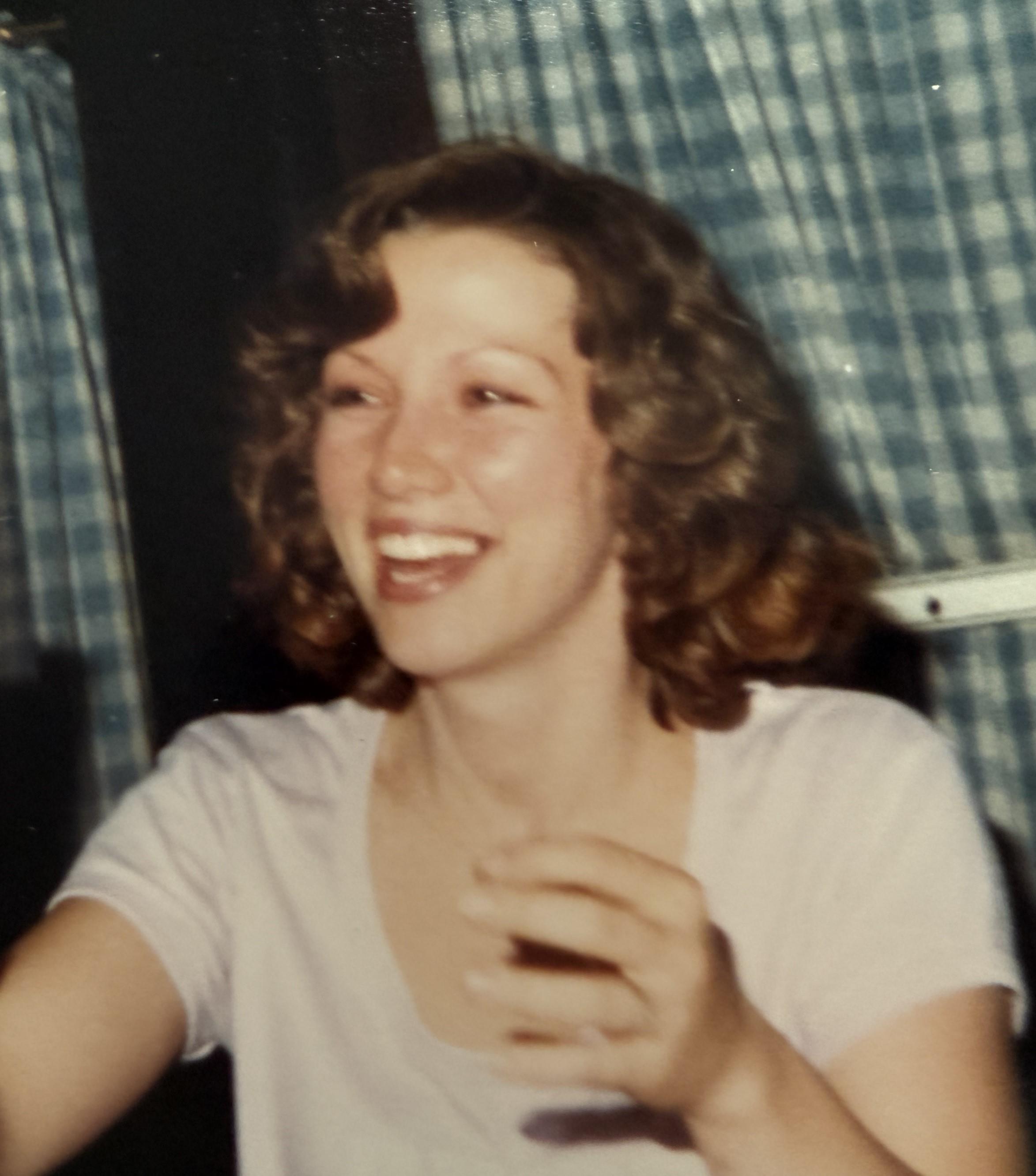 Smiling young woman has a joyful expression while engaging with friends at an indoor event.