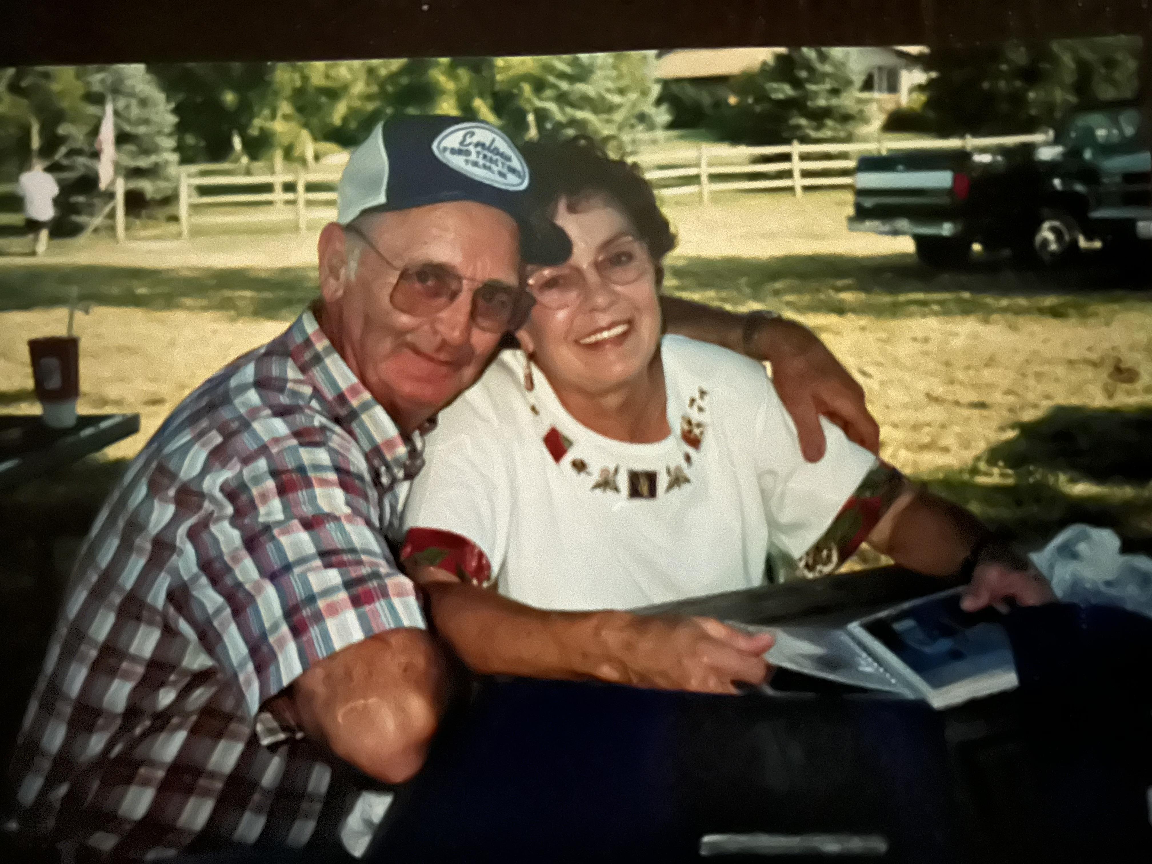 Elderly couple smiles as they relax at a picnic table under shelter in a rural area.