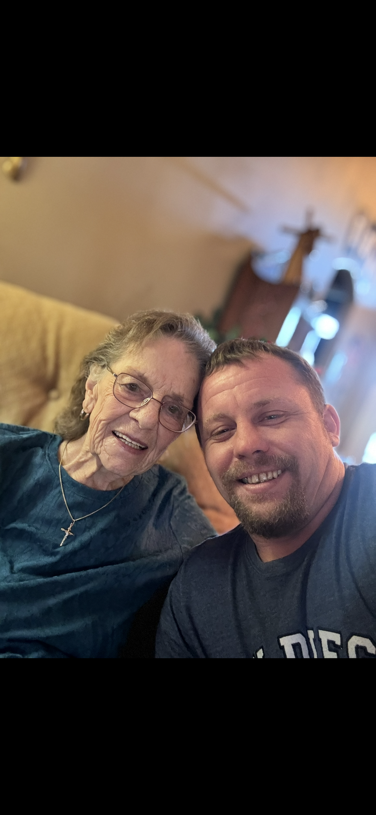 A man and an elderly woman smile together in a warm, inviting living room, showcasing their bond.
