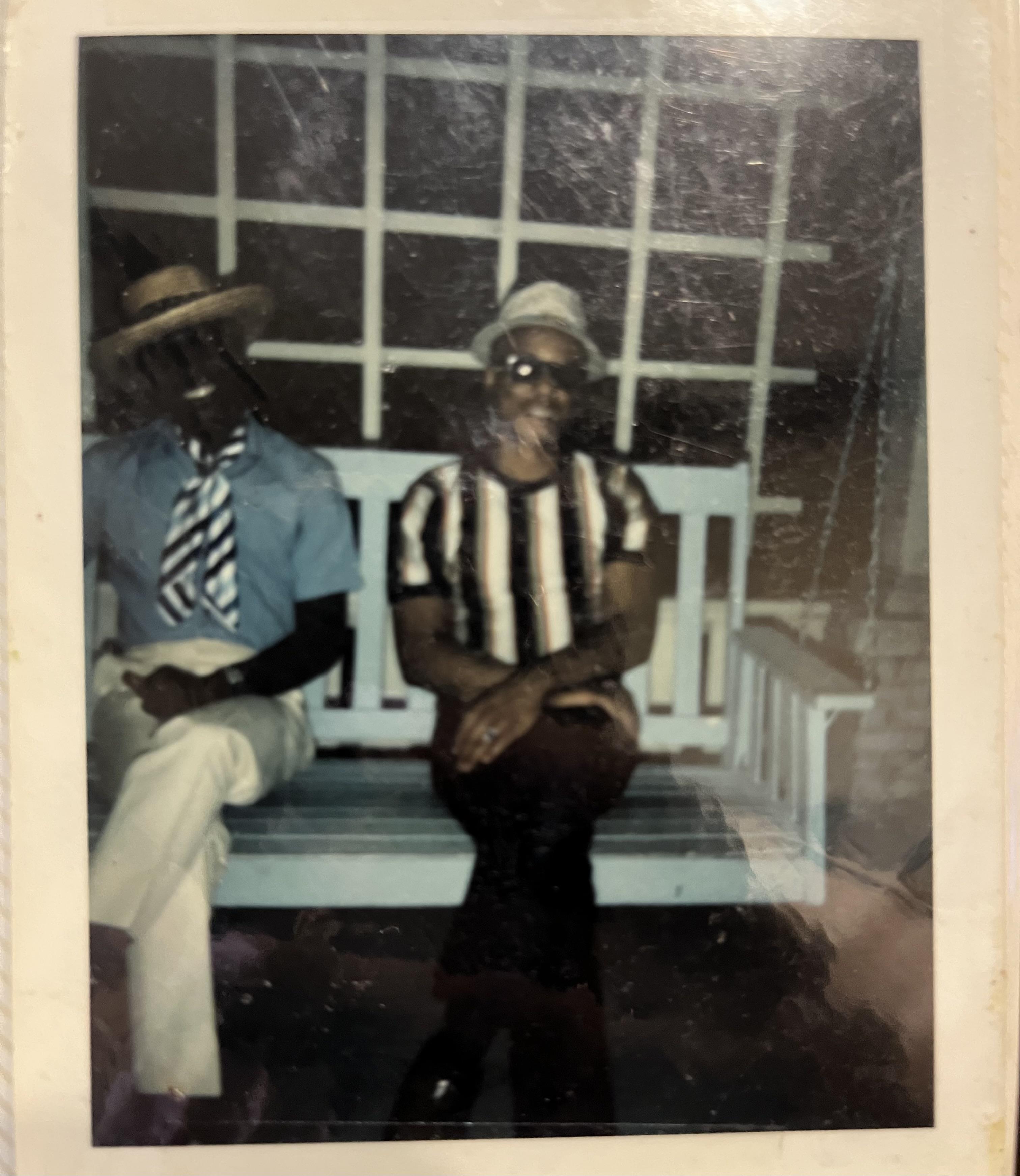 Two fashionable men relax on a wooden bench, showcasing their unique styles in a cozy setting.