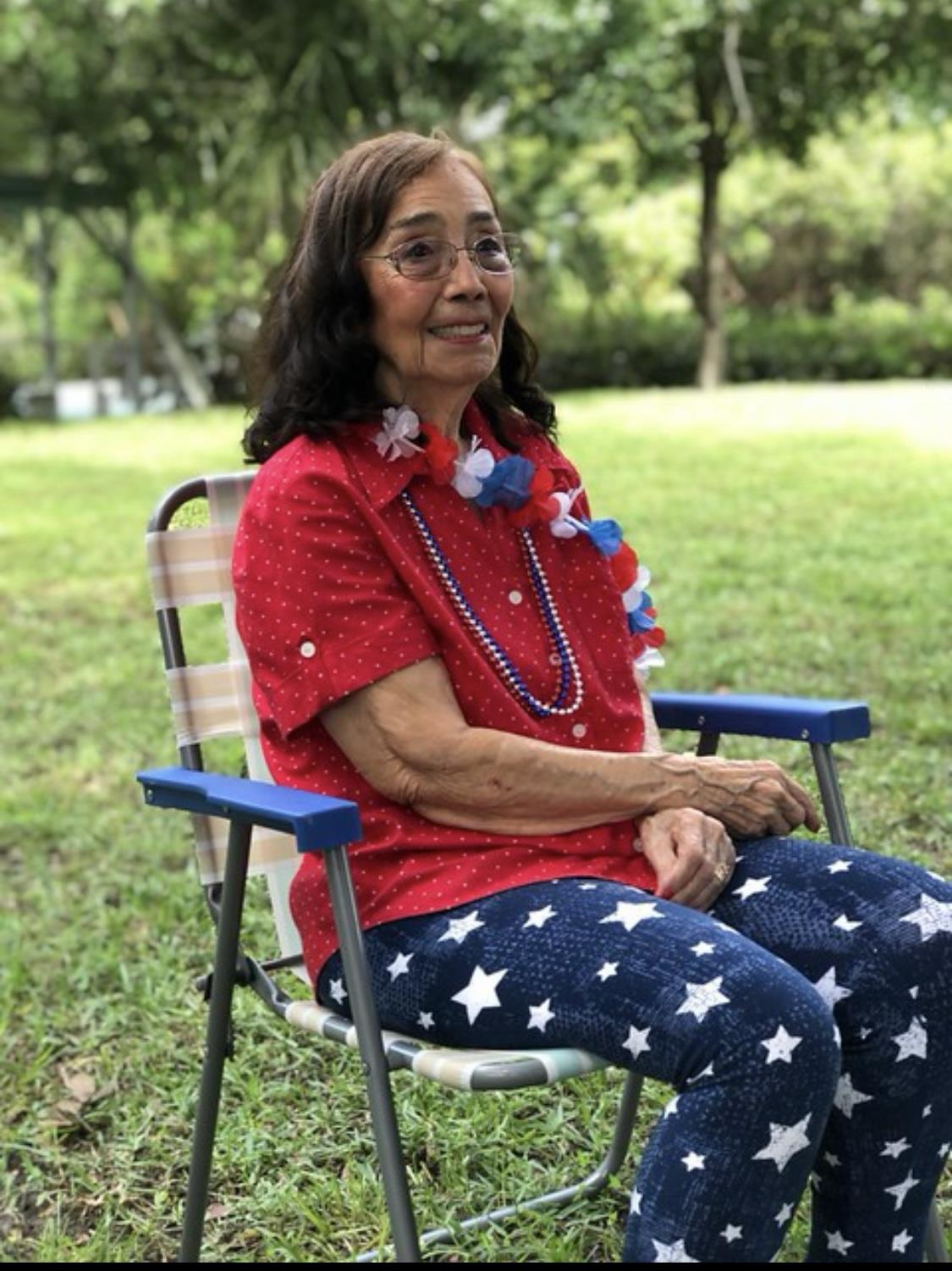 A woman sits comfortably in a chair wearing a vibrant outfit adorned with festive accessories.