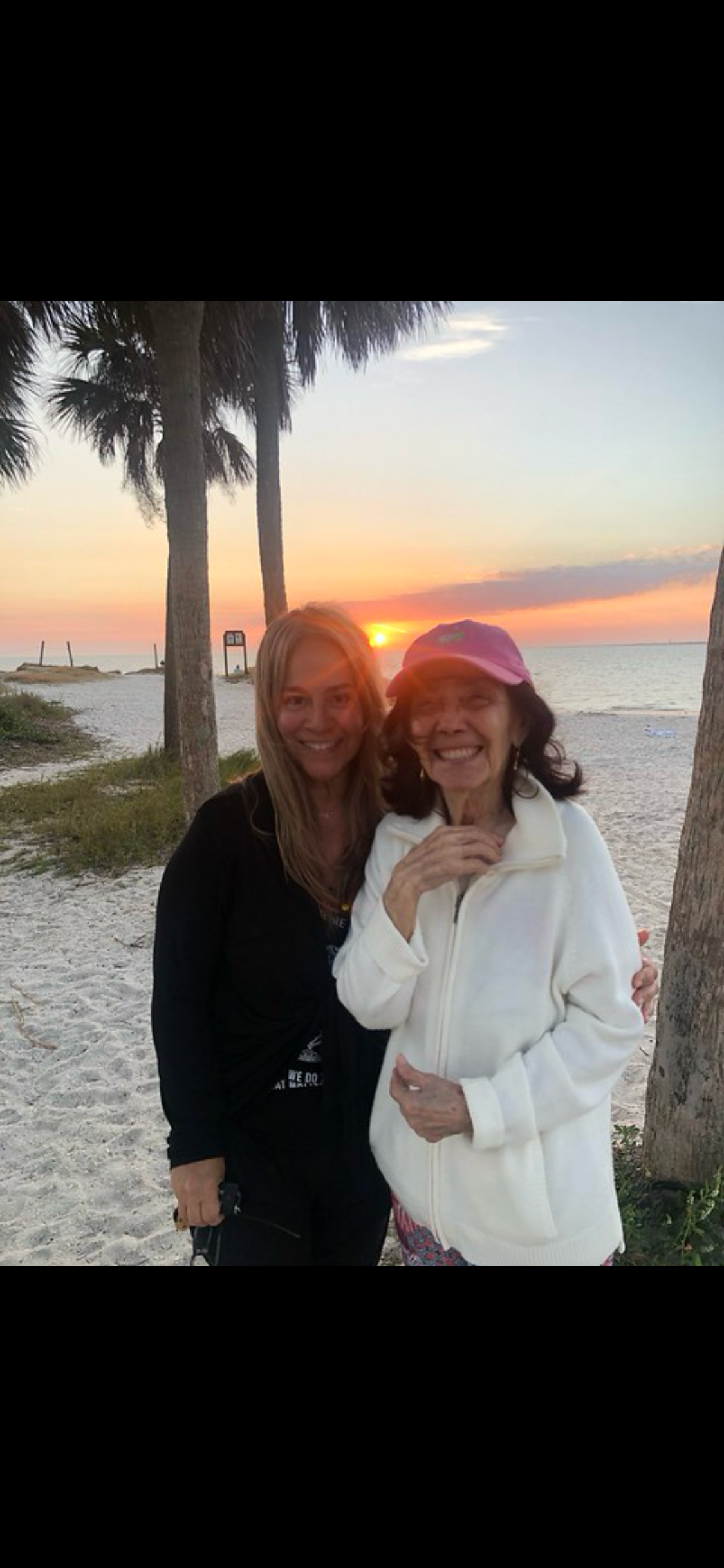 Two women enjoy a joyful moment on the beach as the sun sets over the water.