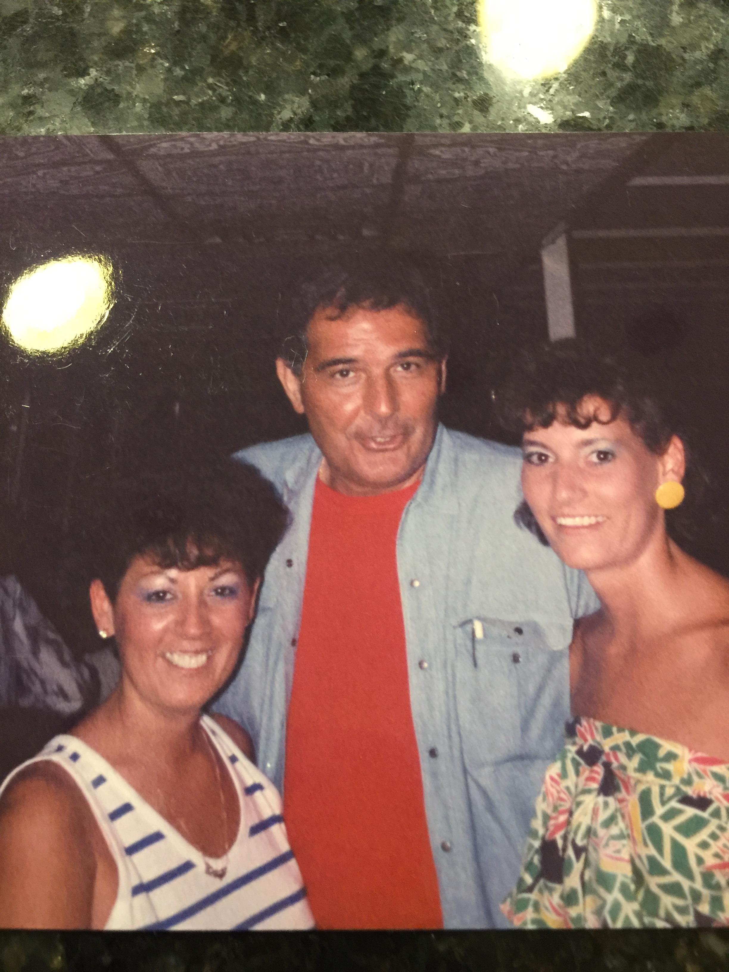 Three friends pose closely, smiling joyfully at a social event during the evening.