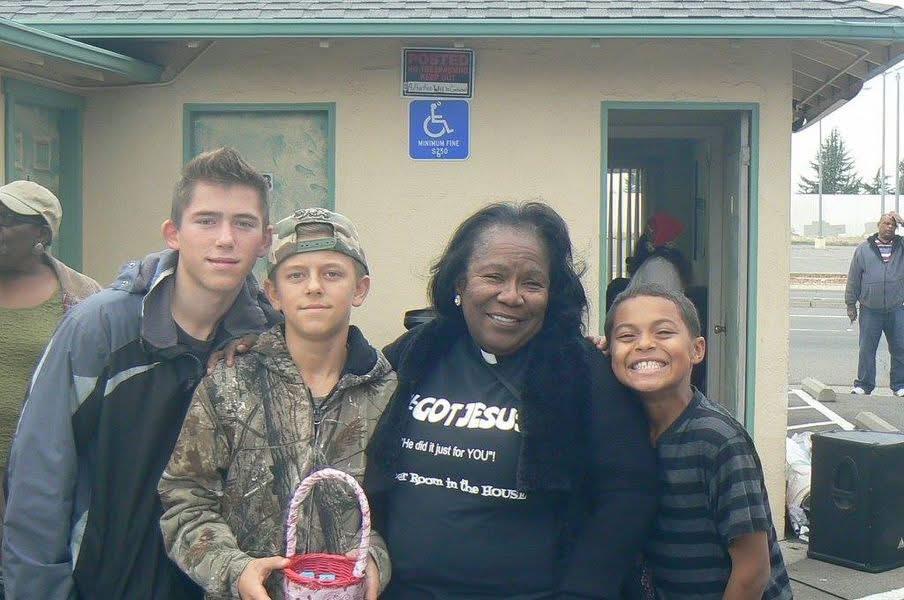 Children of various ages stand with a woman, all smiling and enjoying their time together outdoors.
