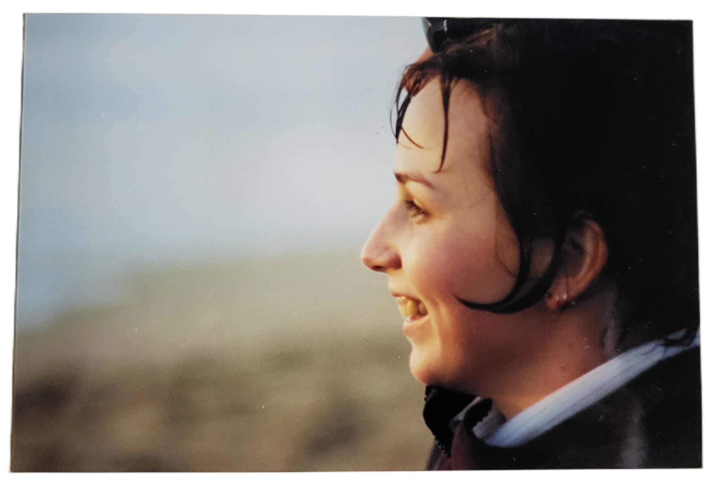 A woman enjoys a serene moment by the coast at sunset, her smile radiating warmth and joy.